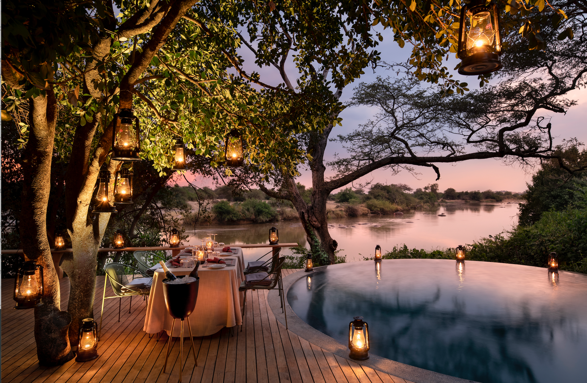 A table and chairs on a deck overlooking a swimming pool at a lodge in Africa.