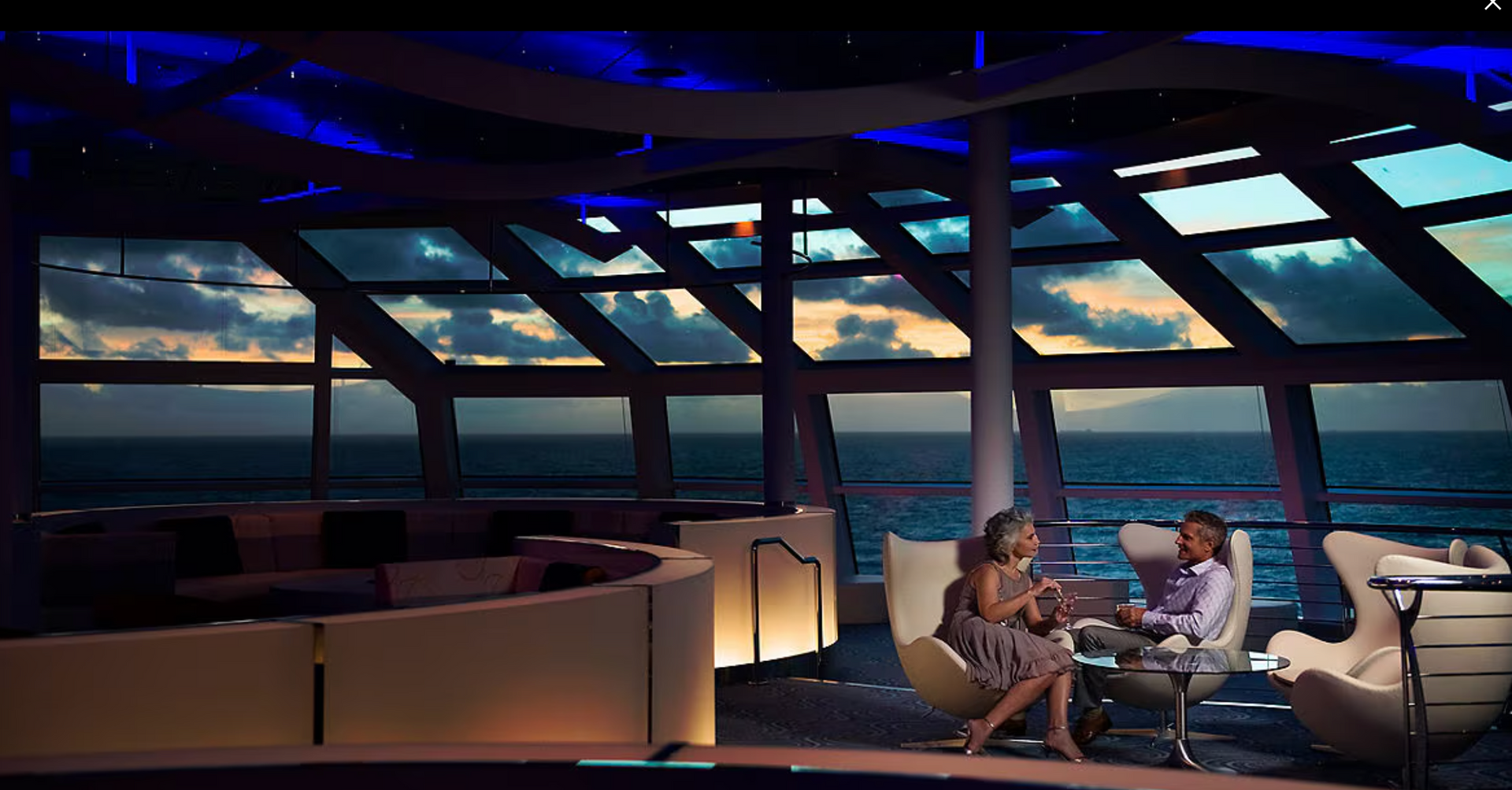 A man and a woman are sitting in a room with a view of the ocean on the Celebrity Solstice cruise ship.