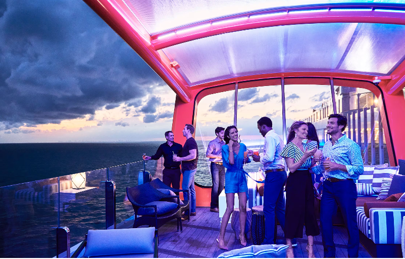 A group of people are standing on a balcony overlooking the ocean on the Celebrity Xcel cruise ship.