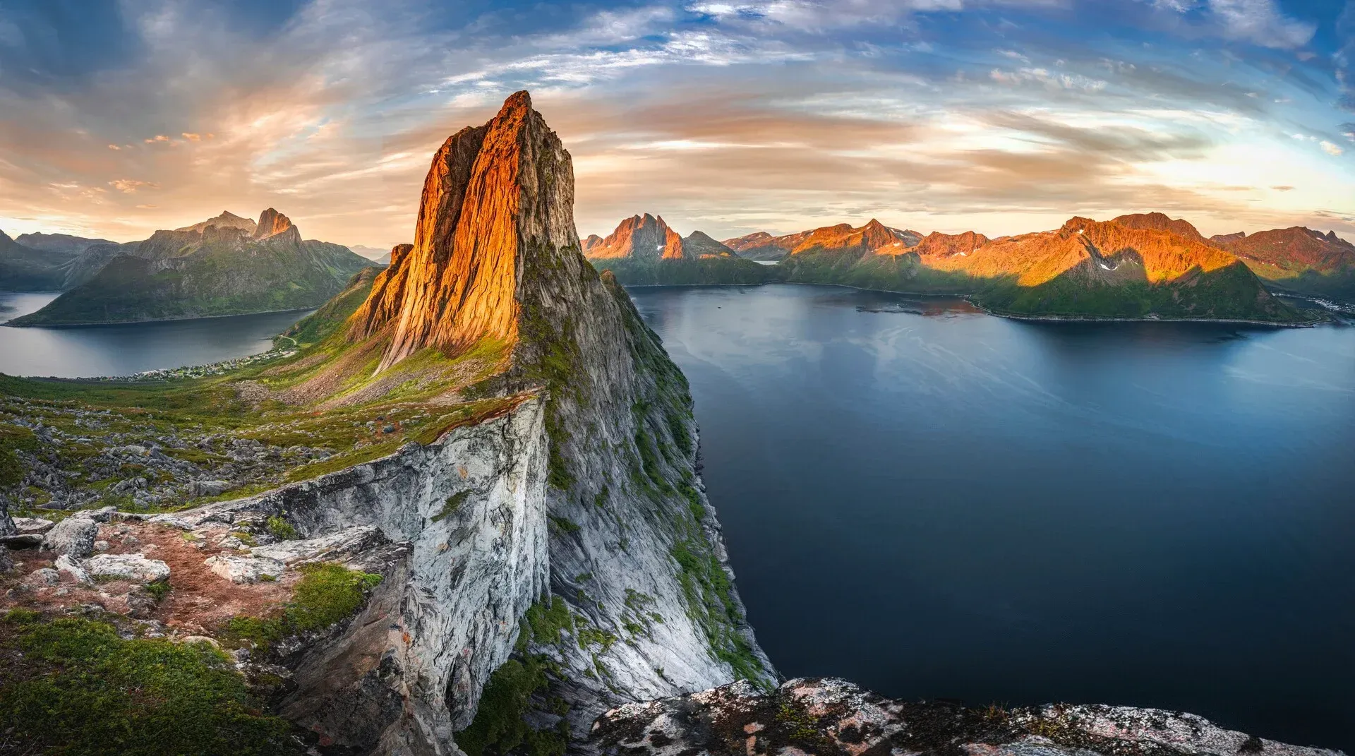 A mountain sitting on top of a cliff overlooking a body of water in Senja, Norway.