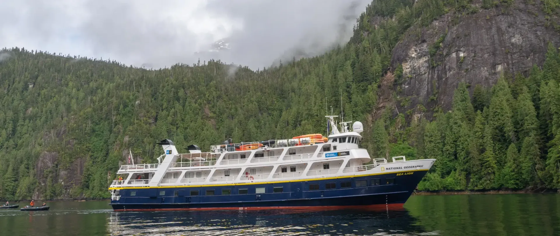Lindbad's Sea Lion  Expedition Cruise ship is floating on top of a lake surrounded by trees.