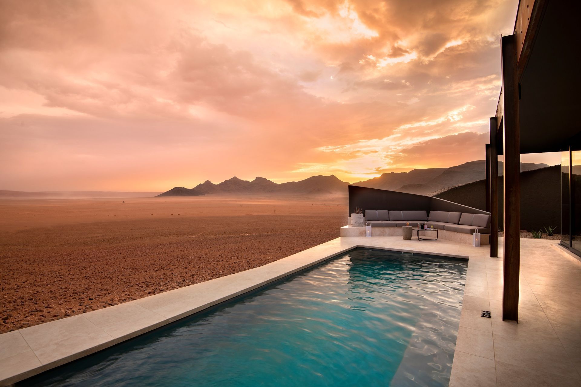 A swimming pool with a view of an African desert at sunset at a lodge.