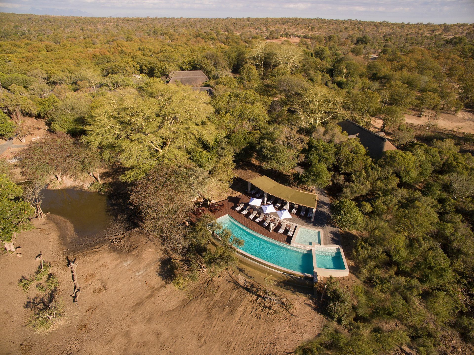 An aerial view of a swimming pool in the middle of a forest in Africa.