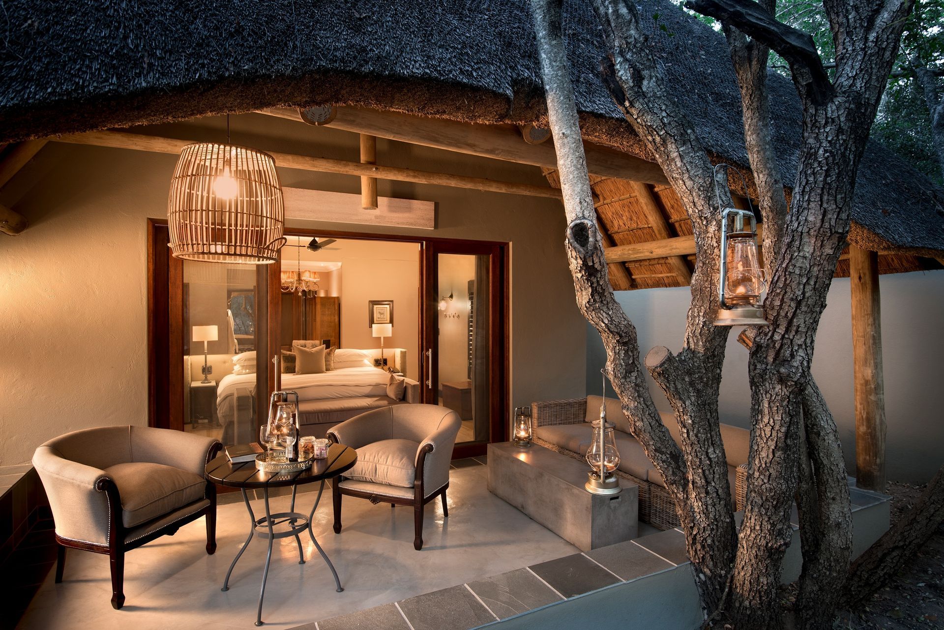 A lodge with a thatched roof has a patio area with chairs and a table in Africa.