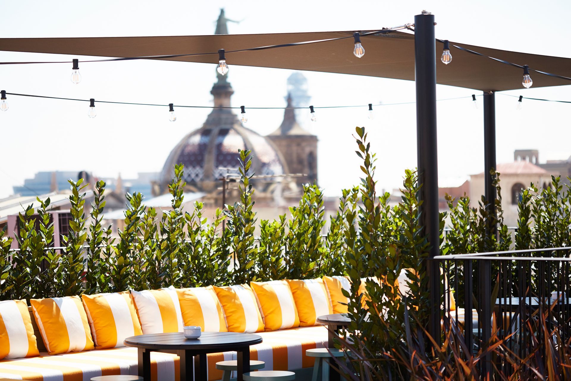 A patio with a striped couch and tables with a dome in the background at Wittmore Hotel in Barcelona, Spain.