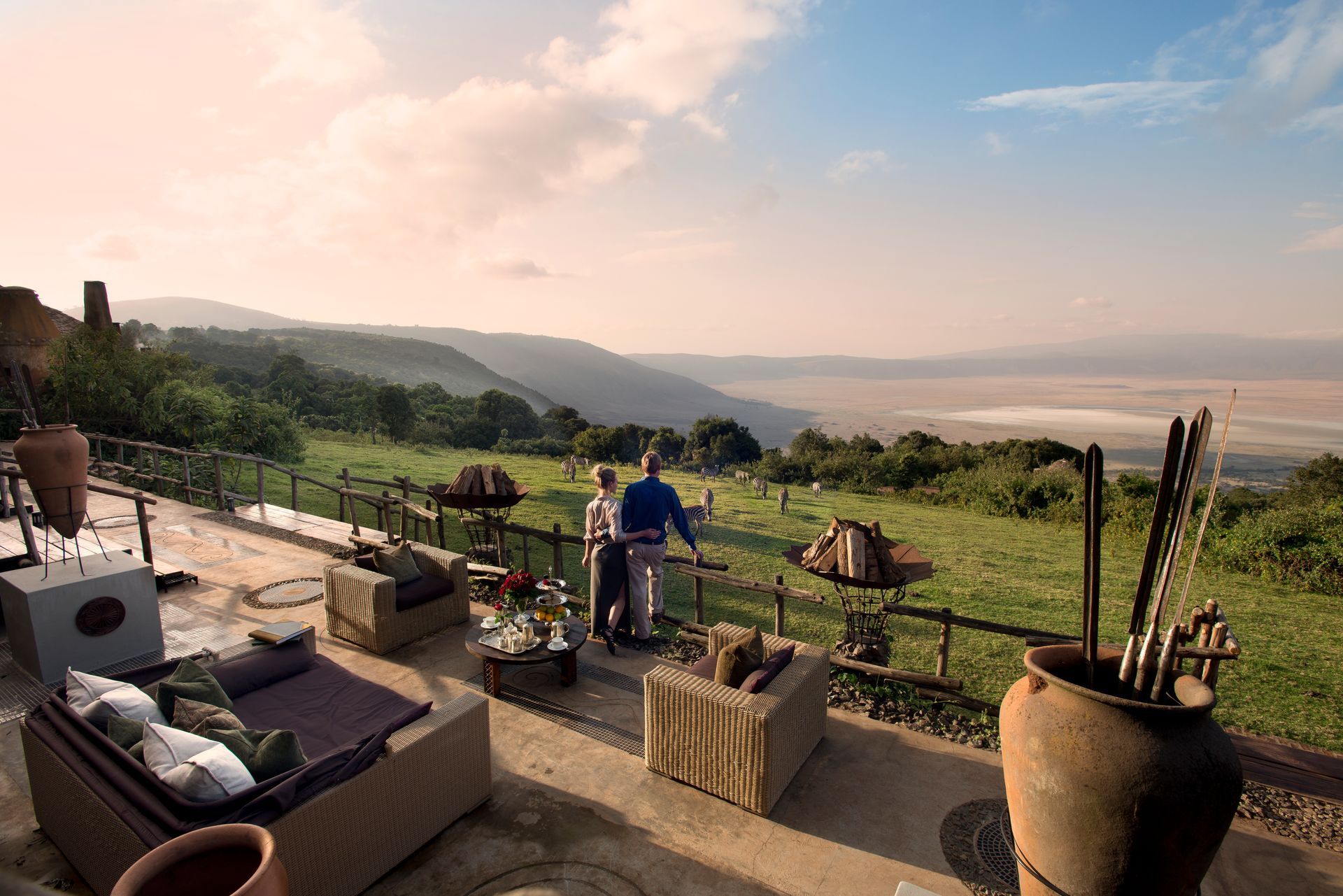 A couple standing on a balcony overlooking a lush green field at a camp in Africa.