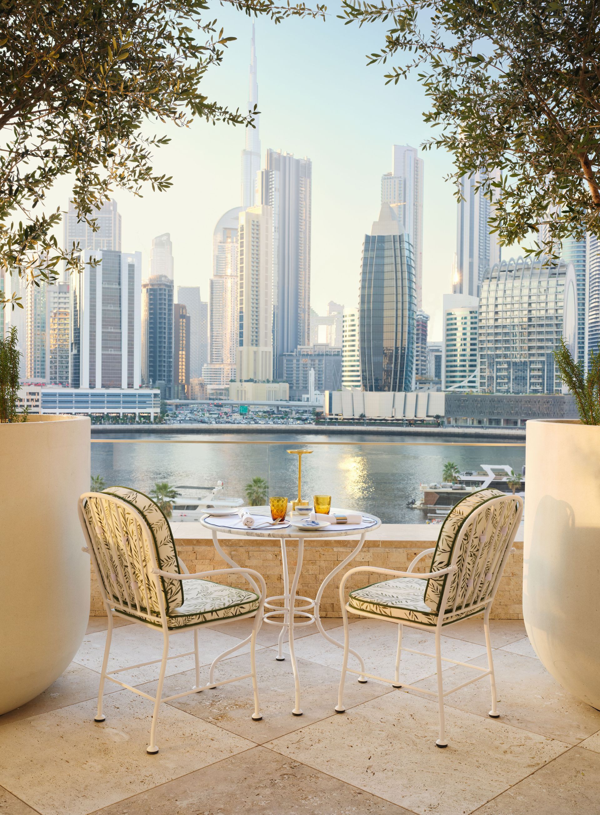 A table and chairs on a balcony overlooking a city skyline at the Dorchester Collection Hotel in Dubai.