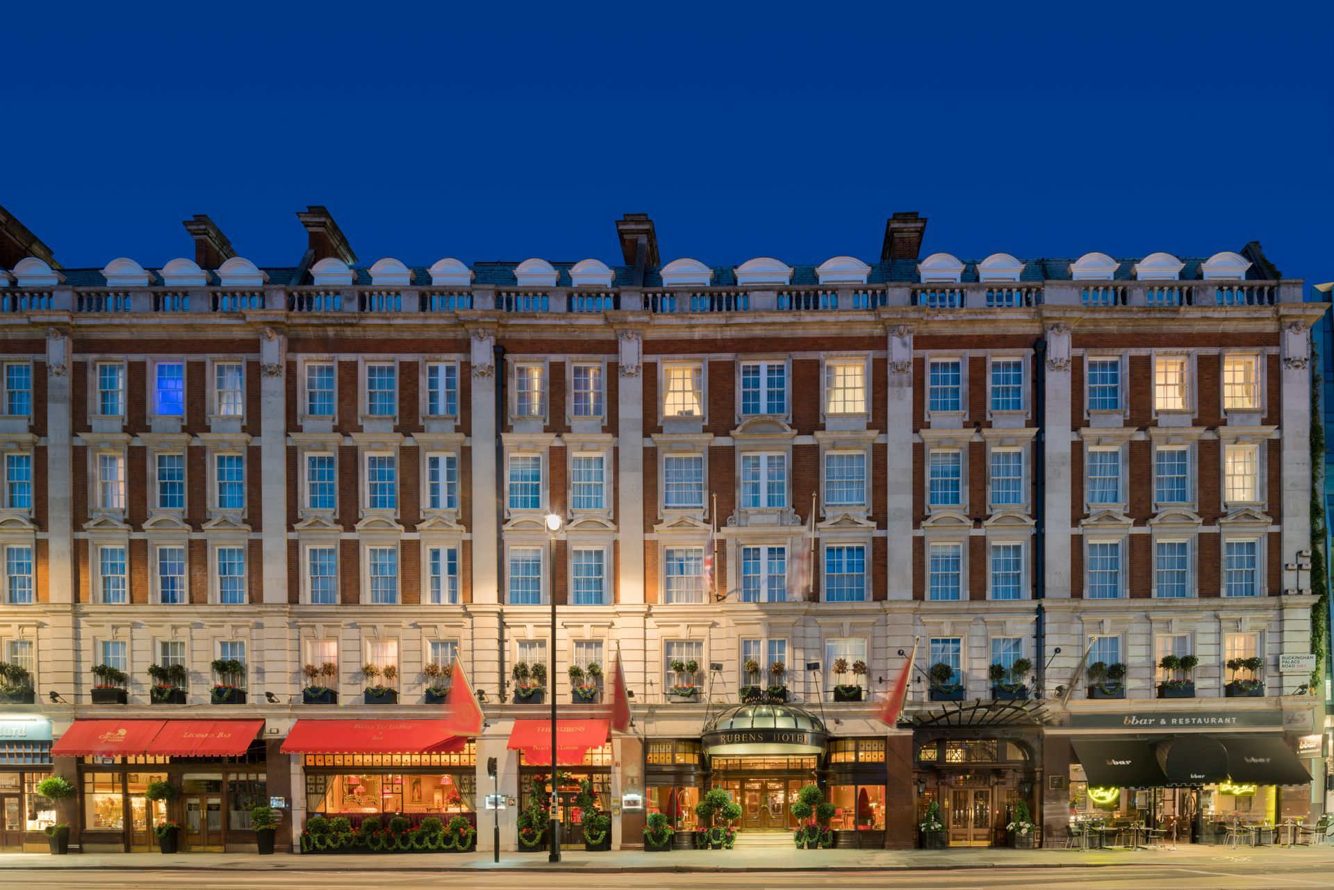A large brick hotel with a lot of windows is lit up at night at the London Red Carnation Hotel.
