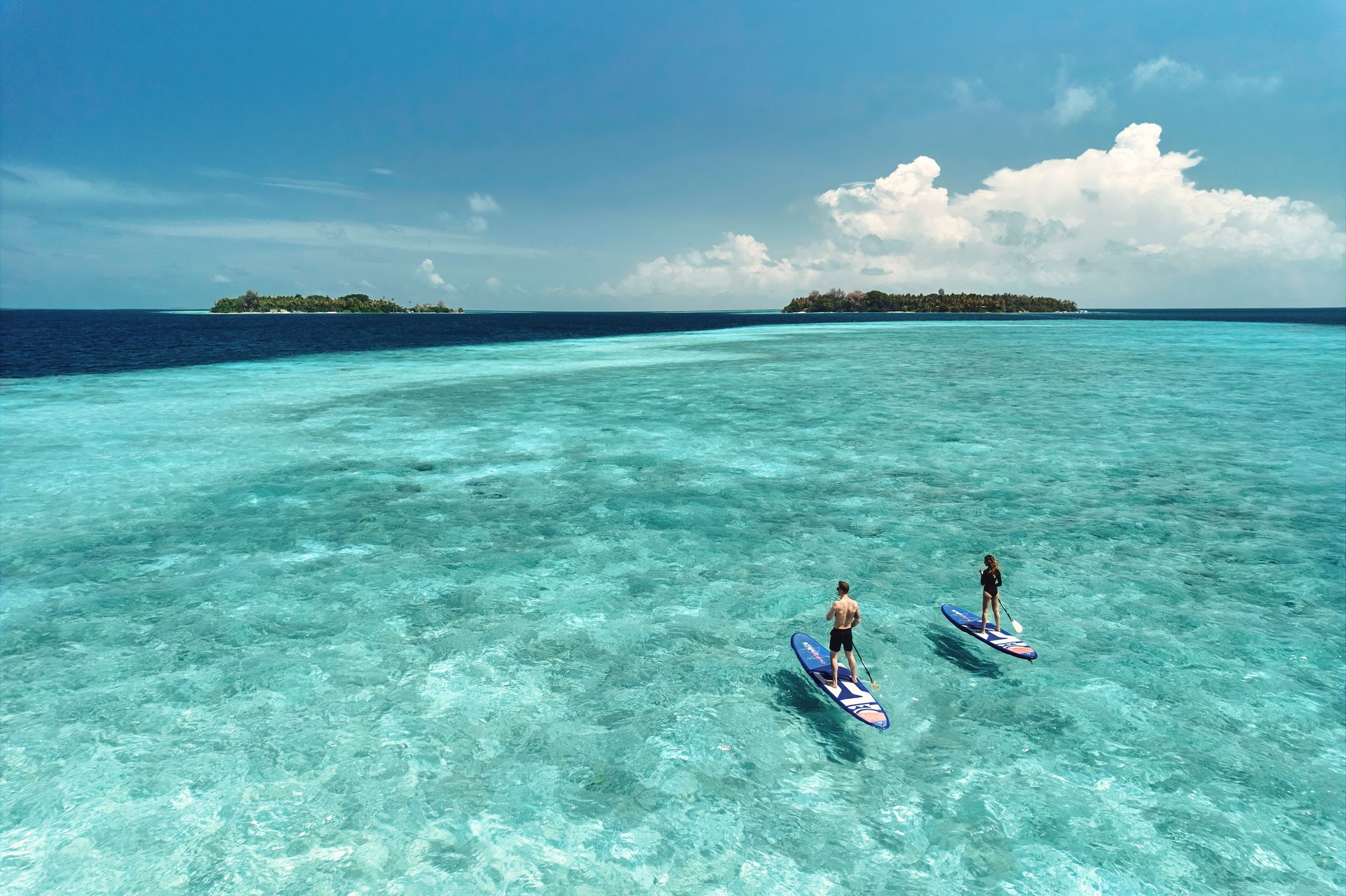 A couple of people are riding kayaks in the ocean in the maldives. 