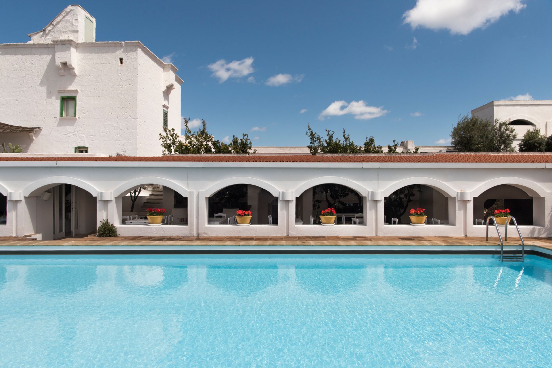 A large swimming pool in front of a white building at Il Melograno Hotel in Puglia, Italy.