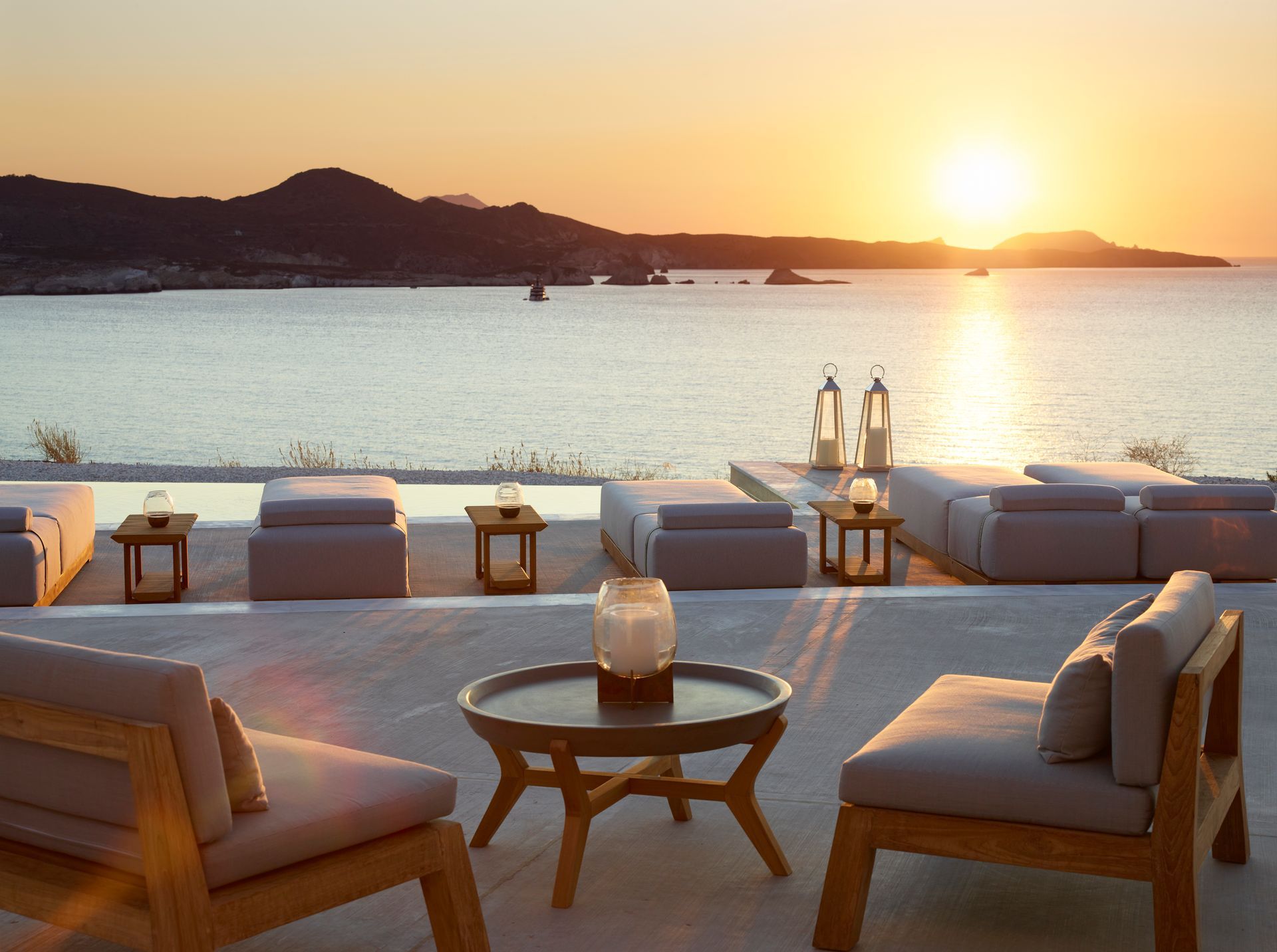 A patio with chairs and a table overlooking the ocean at sunset at Domes White Coast Hotel in Milos, Greece.