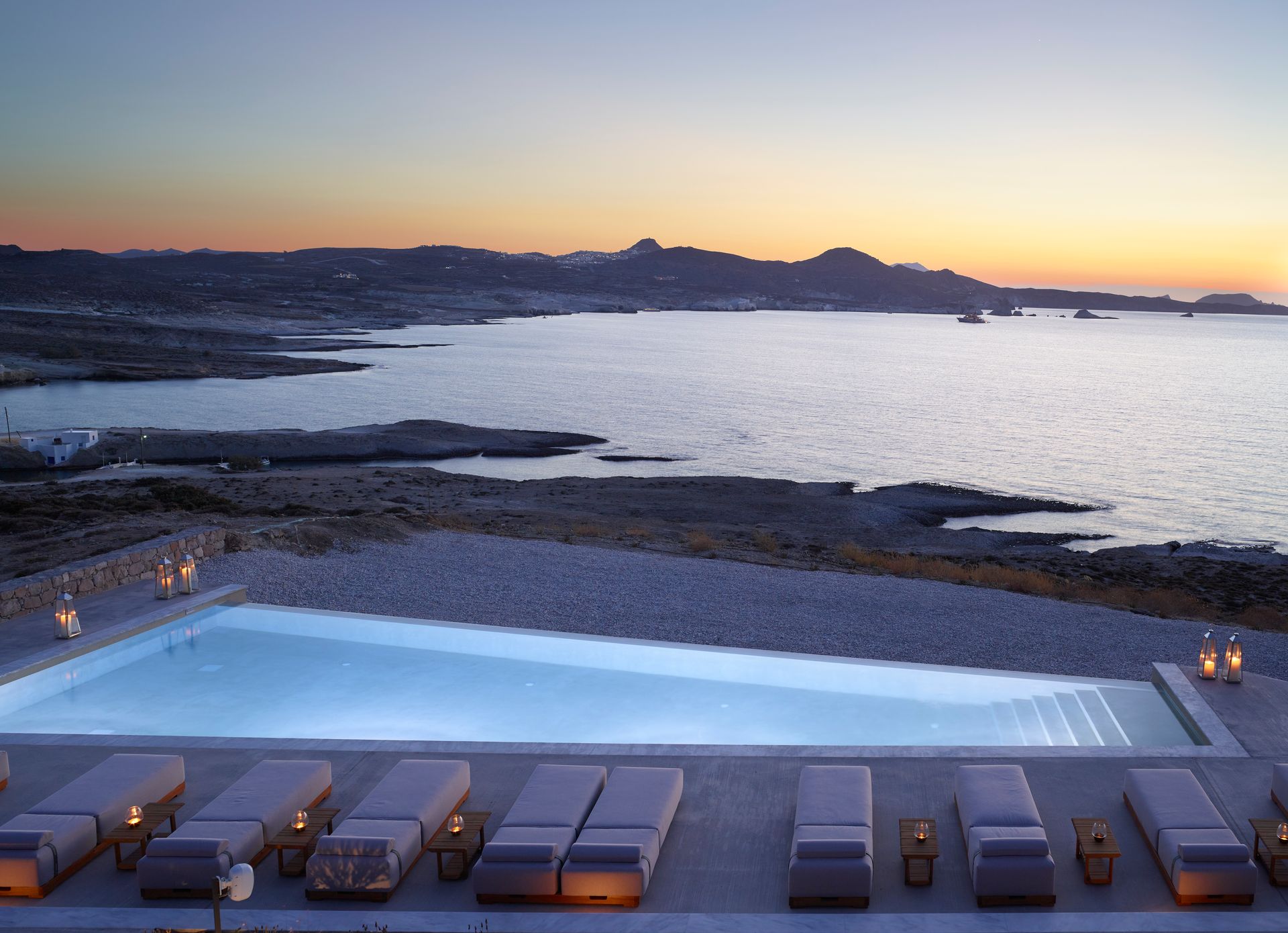 A large swimming pool with a view of the ocean at sunset at Domes White Coast Hotel in Milos, Greece.