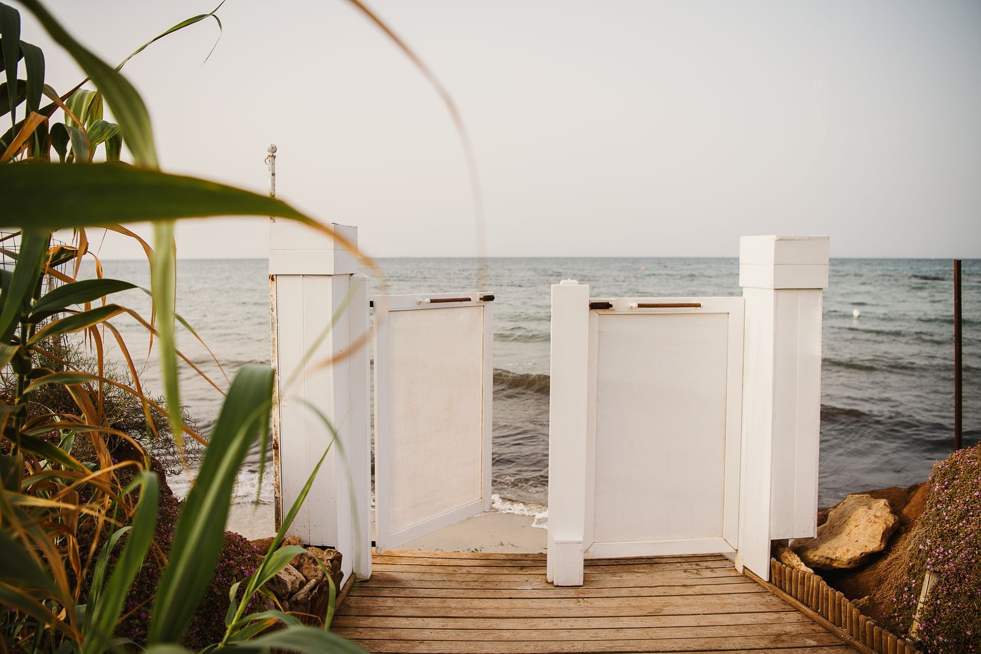 A wooden walkway leading to the ocean with a white gate at Canne Bianche Lifestyle Hotel in Puglia, Italy.