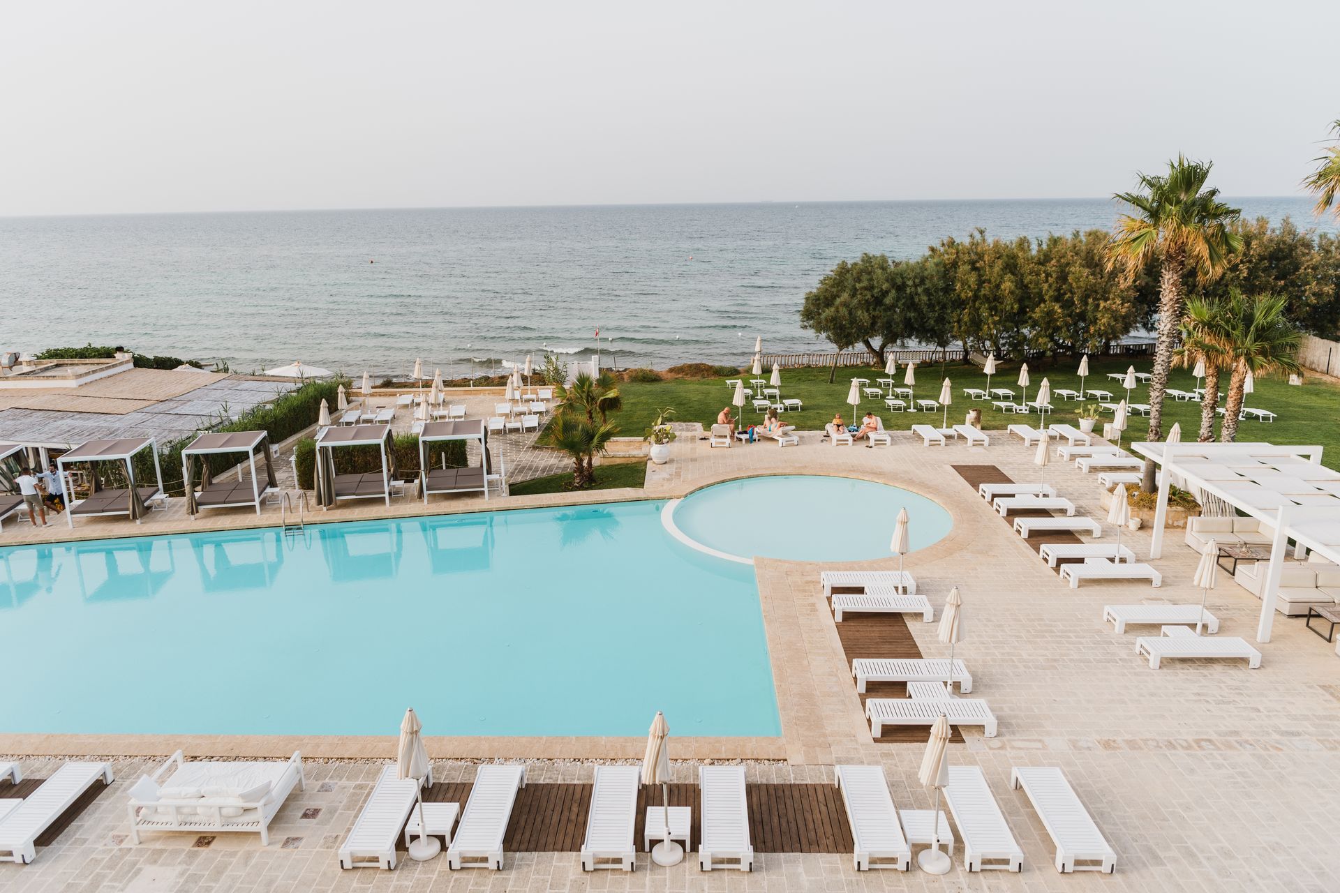 A large swimming pool surrounded by chairs and umbrellas next to the ocean at Canne Bianche Lifestyle Hotel in Puglia, Italy.