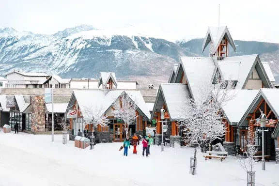 A group of people are walking through a snowy village in Jasper with mountains in the background.
