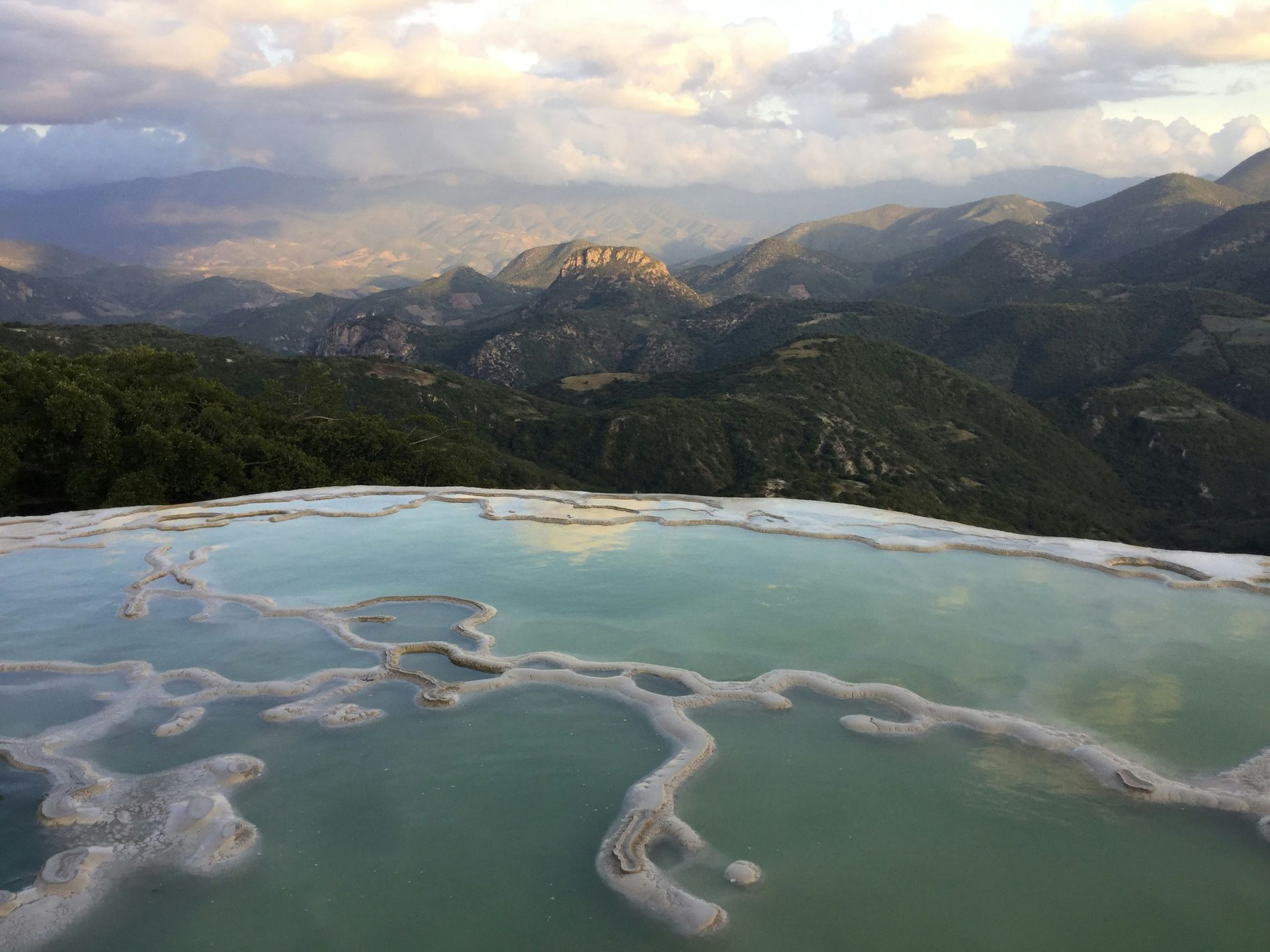 Hierve el Agua, Oaxaca, Mexico: Mineral pools with turquoise water overlook a mountain landscape under a cloudy sky.