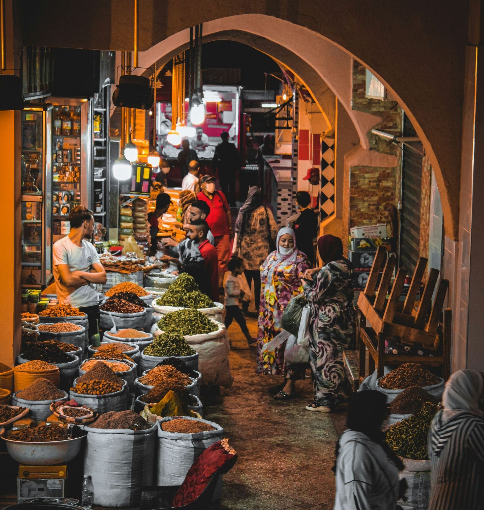 A group of people are standing in a market at night in Morocco.