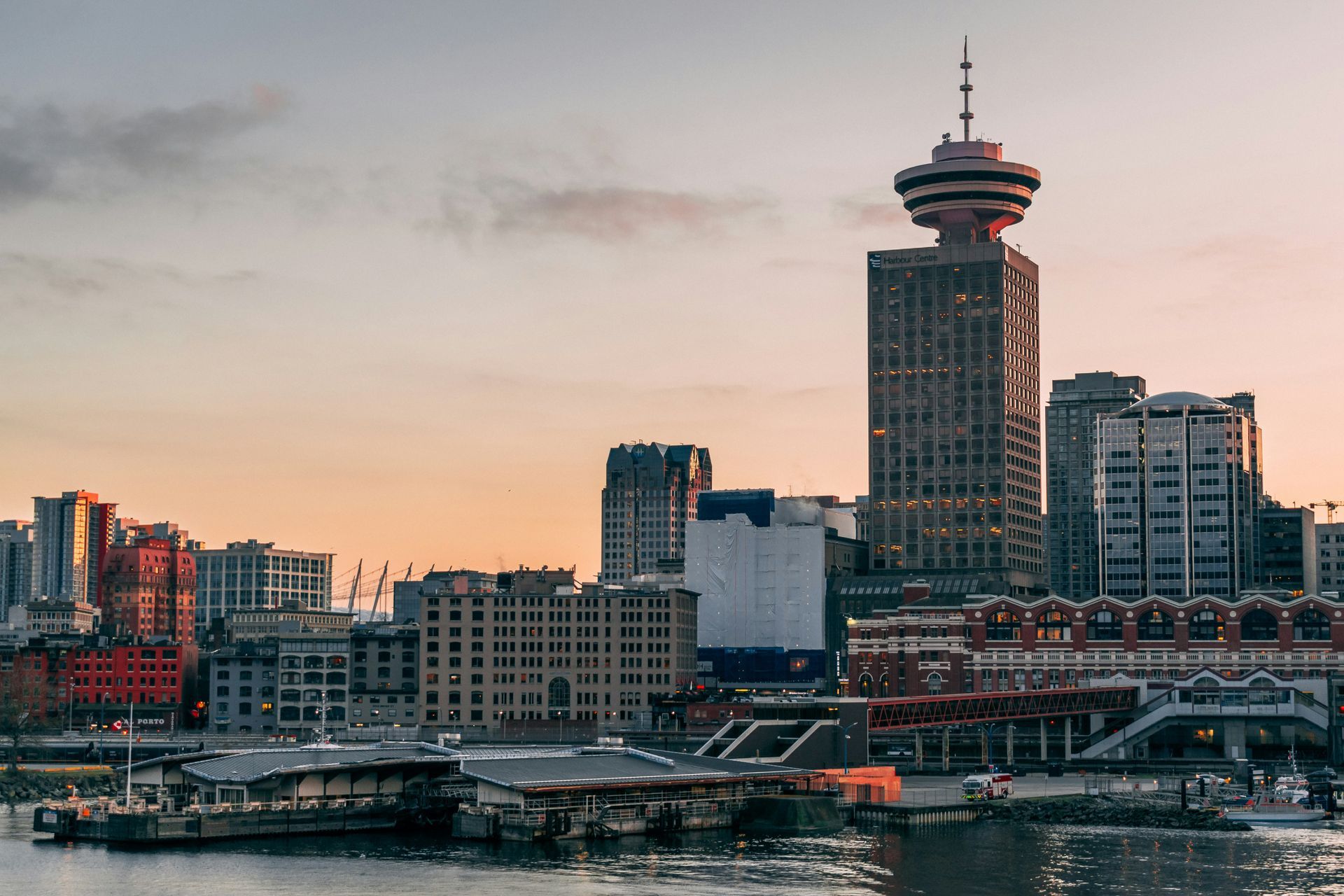 Skyline of Vancouver, Canada, at sunset, with the tall, distinct Vancouver Lookout tower prominently featured.