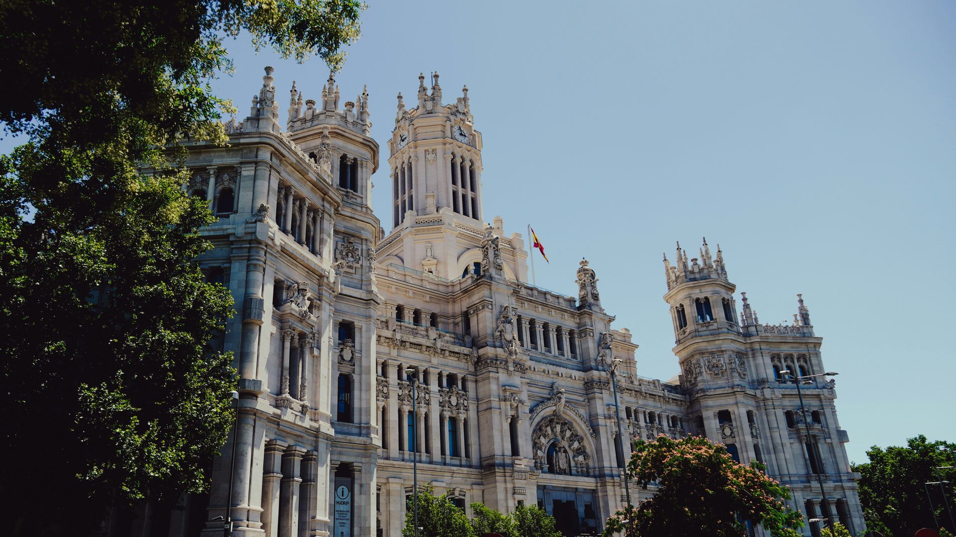 Ornate white Palacio de Cibeles building in Madrid, Spain, under a clear blue sky, with green trees.