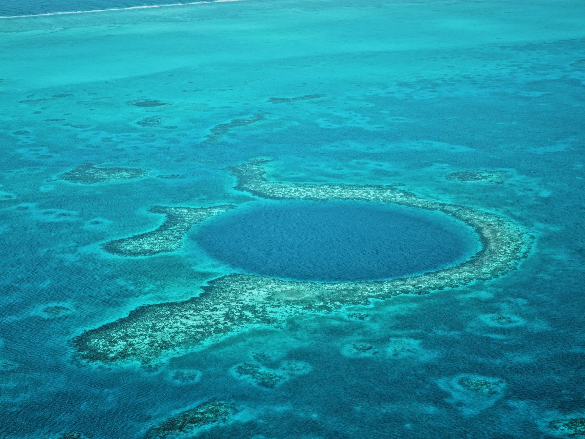Aerial view of the Great Blue Hole in Belize, a large, dark blue sinkhole surrounded by coral reefs in turquoise waters.