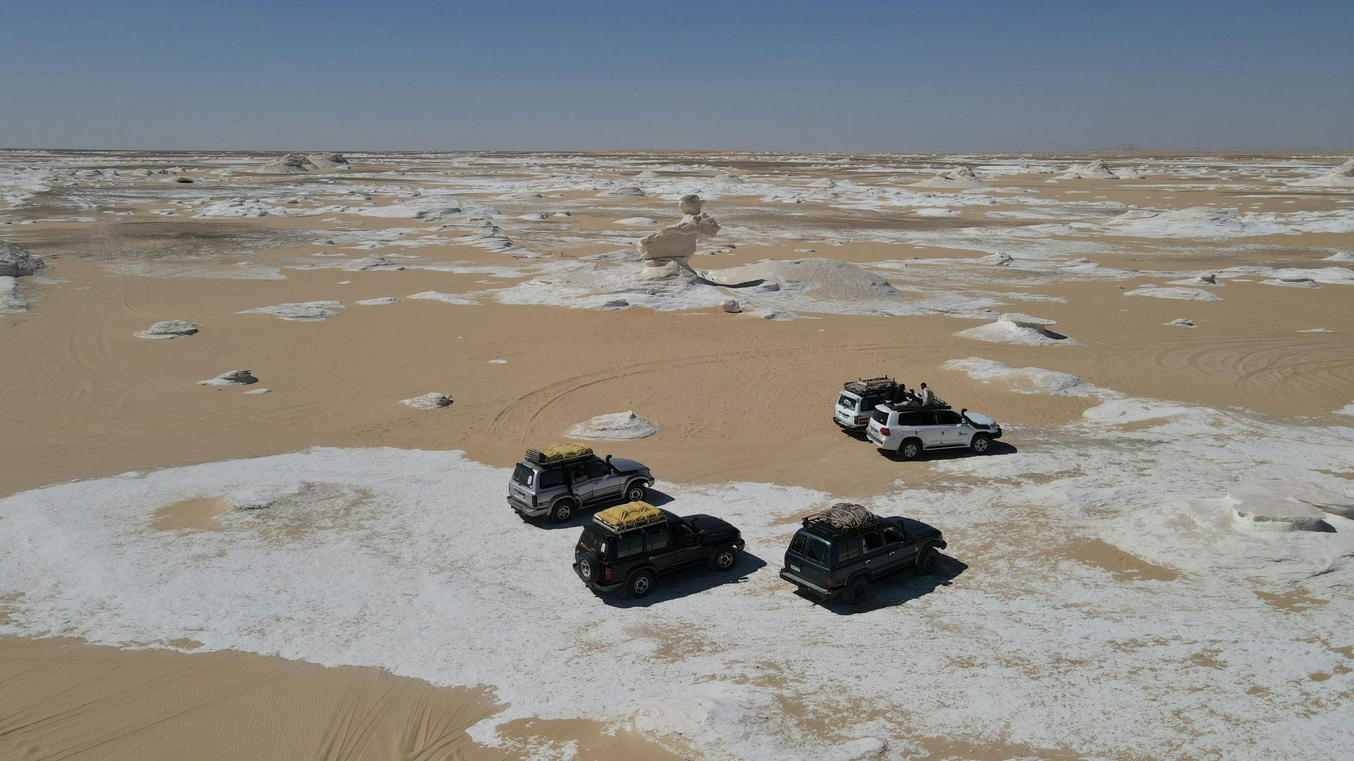 Three cars are parked in the sand in White Desert National Park in Egypt.