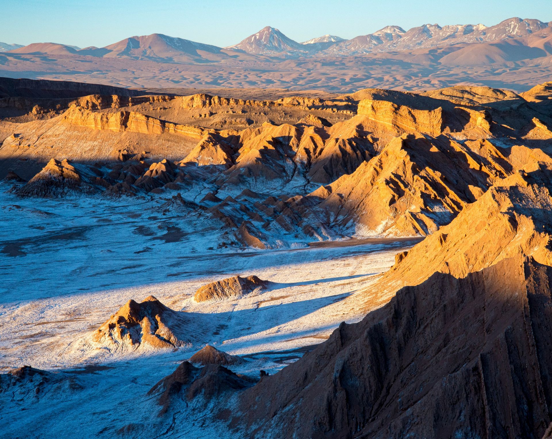 Desert landscape with sunlit canyons and snow-covered flats, mountains in the background in the Atacama Desert, Chile.