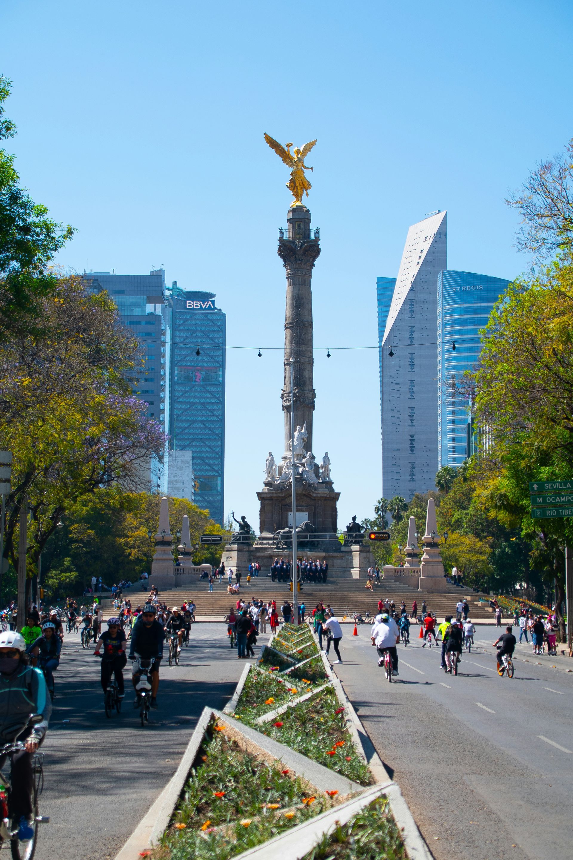 The Angel of Independence monument in Mexico City, a tall column topped with a golden angel statue, surrounded by buildings.