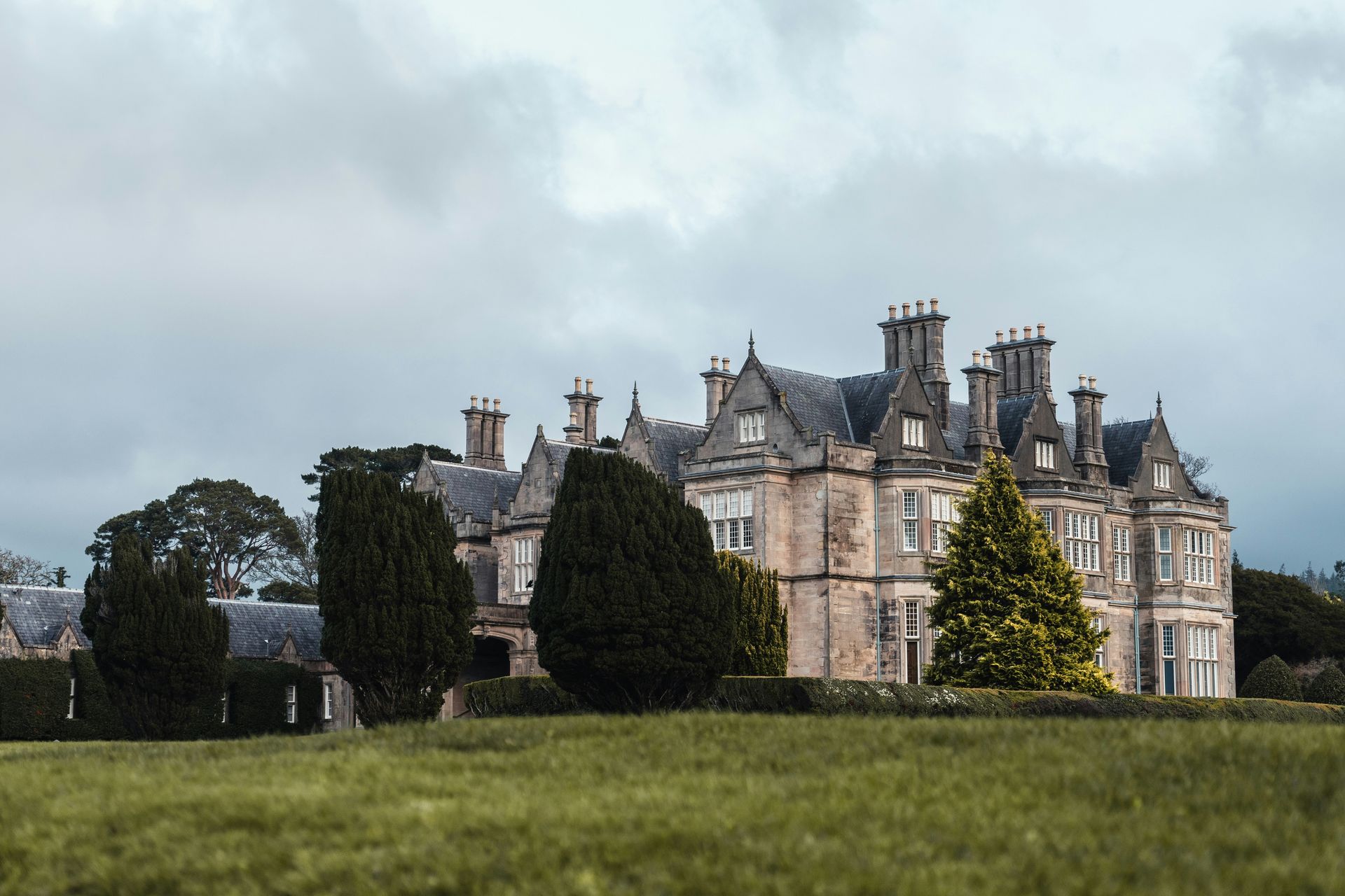 Large stone mansion with multiple chimneys and trees on a green lawn in Killarney, Ireland.