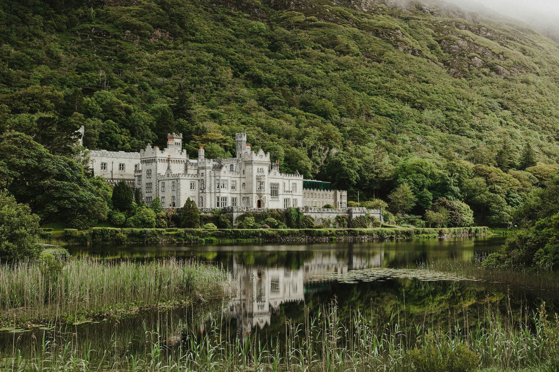 The Kylemore Abbey castle on a lake, surrounded by lush green trees and mountains in Ireland.