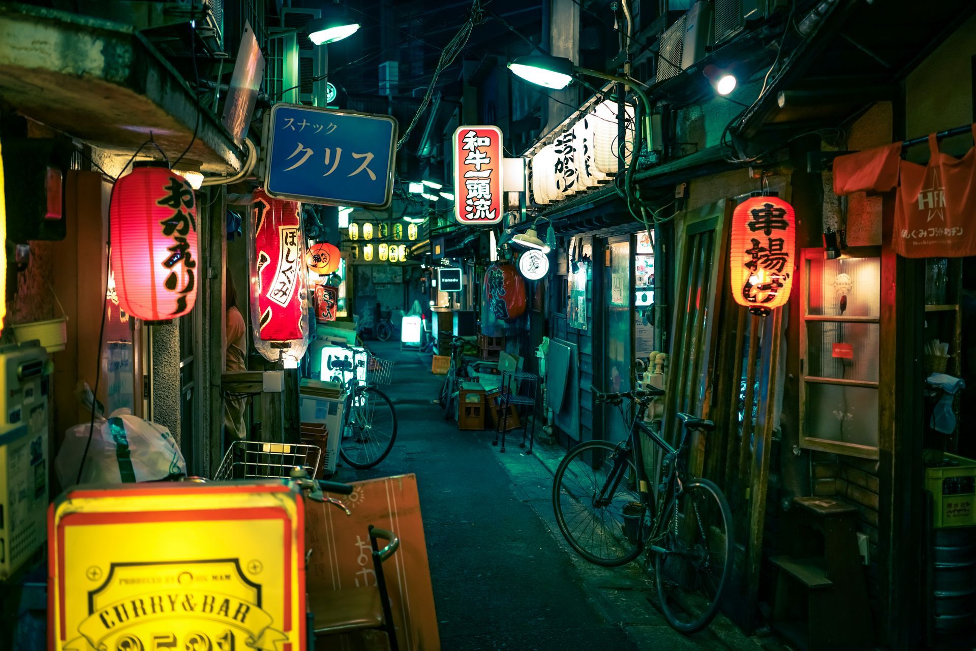 Narrow, neon-lit alley in Japan, with glowing lanterns and storefront signs, bicycles parked along the side.