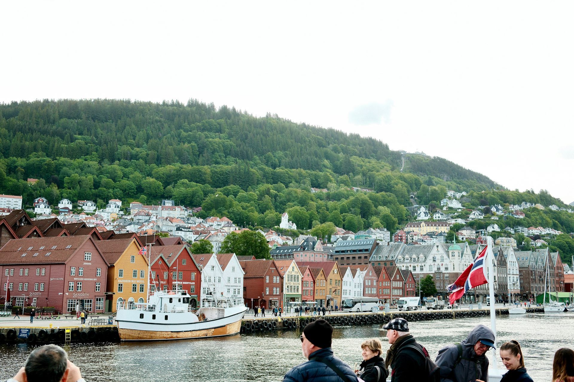 A group of people are standing next to a body of water in front of a city in Bergen, Norway.