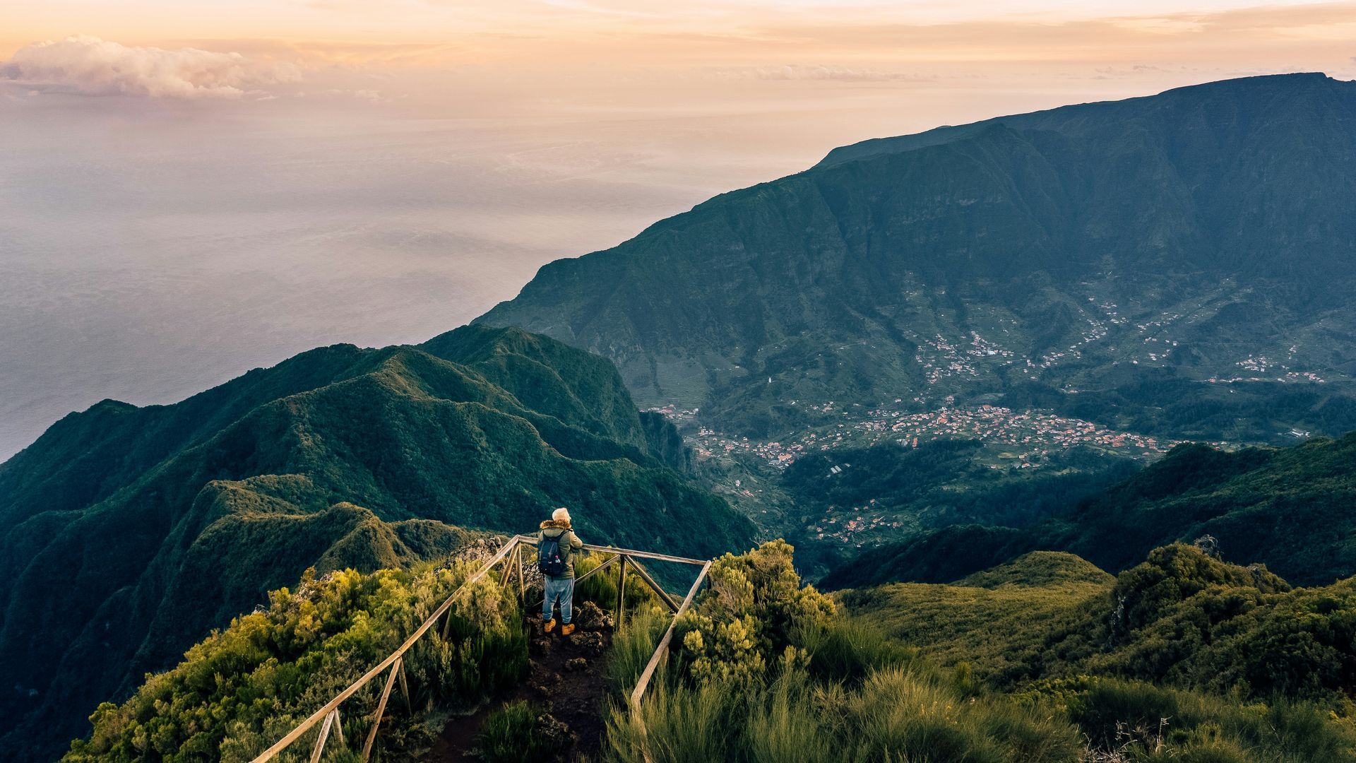 A mountain trail overlooks a valley. Green foliage and distant buildings at sunset on the island of Madeira, Portugal.