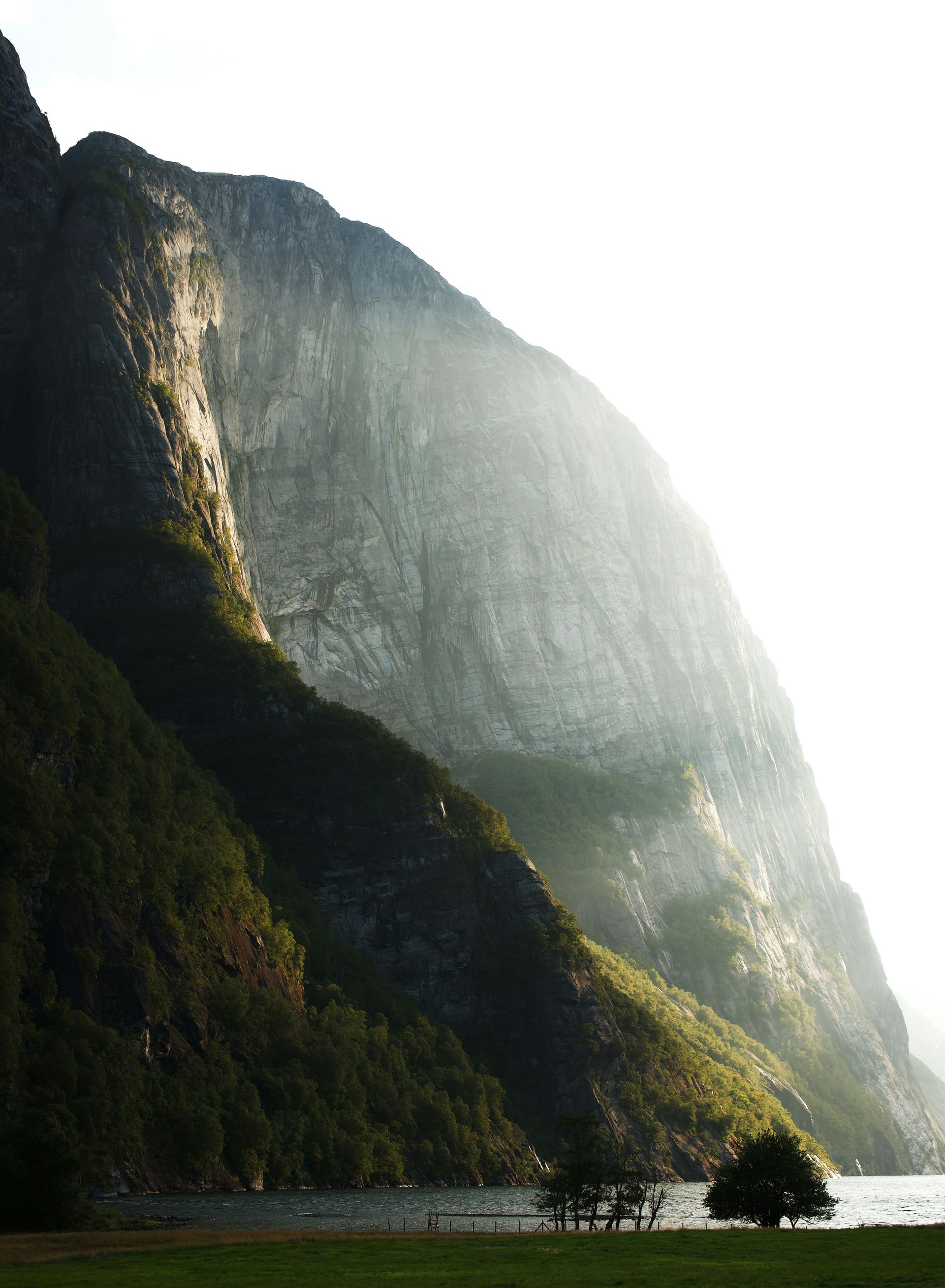Mountain illuminated by sunlight, with lush green hillside, on Lysefjord, Norway.