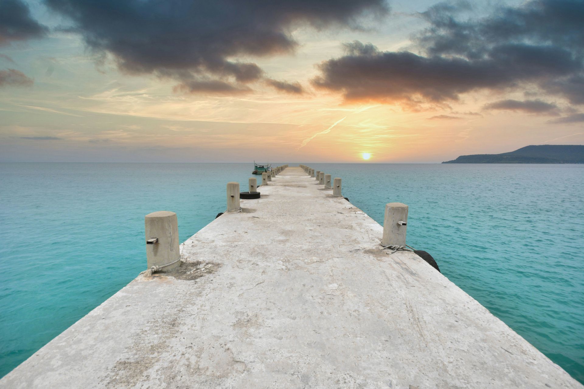 Concrete pier extending into calm turquoise ocean at sunset in Koh Rong, Cambodia.