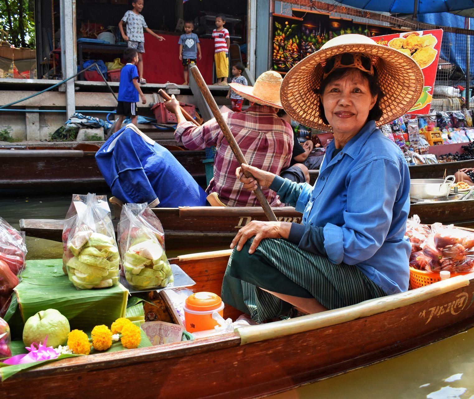 A woman wearing a straw hat is sitting in a boat at the Damnoen Saduak floating market in Thailand.