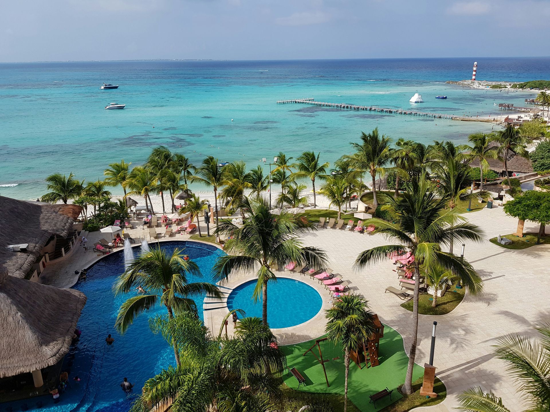 Aerial view of a resort with a turquoise ocean, sandy beach, pools, and palm trees in Cancún, Mexico.
