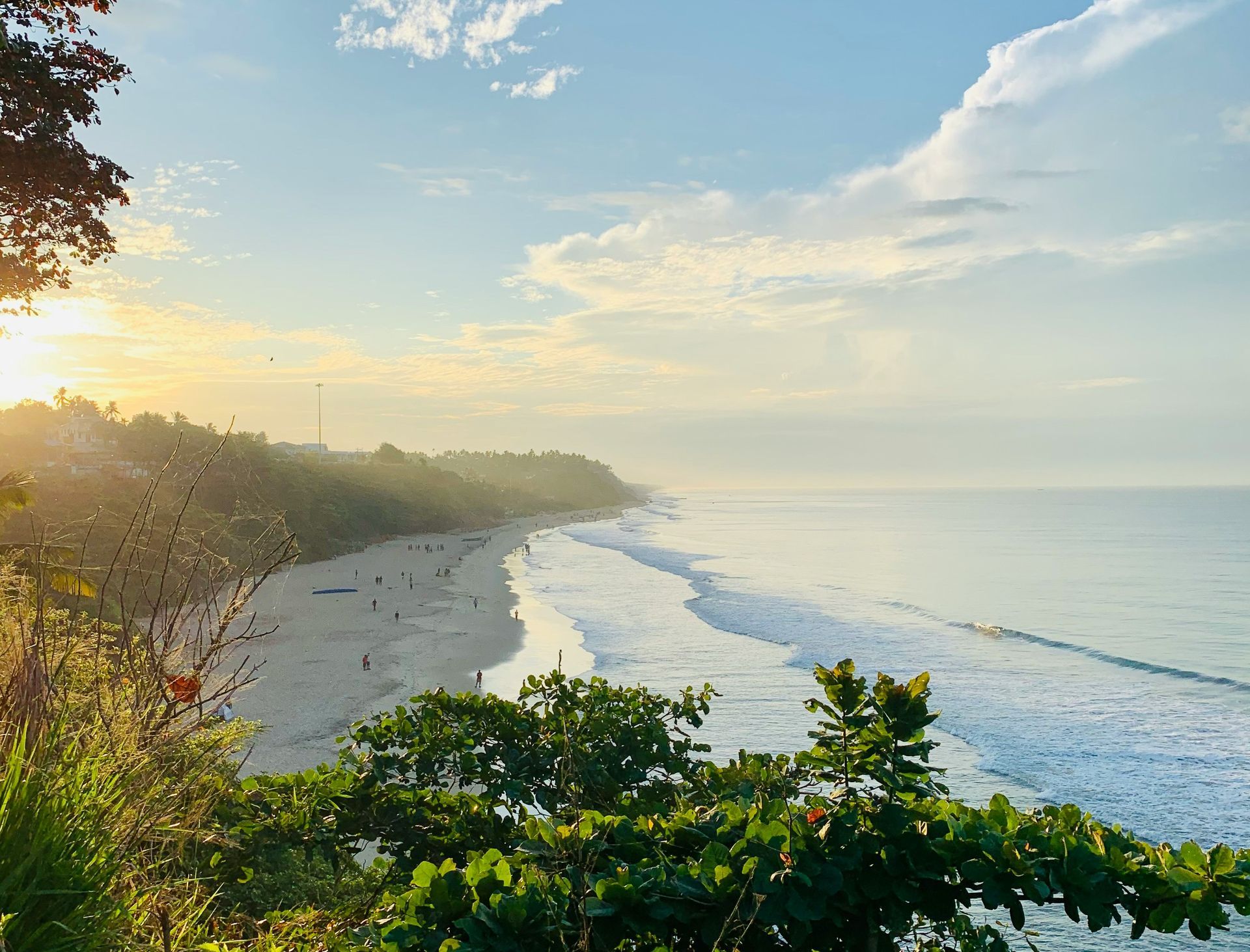 Beach coastline with waves under a bright sky. Sunlight shines on the sandy shore and ocean in Kerala, India.