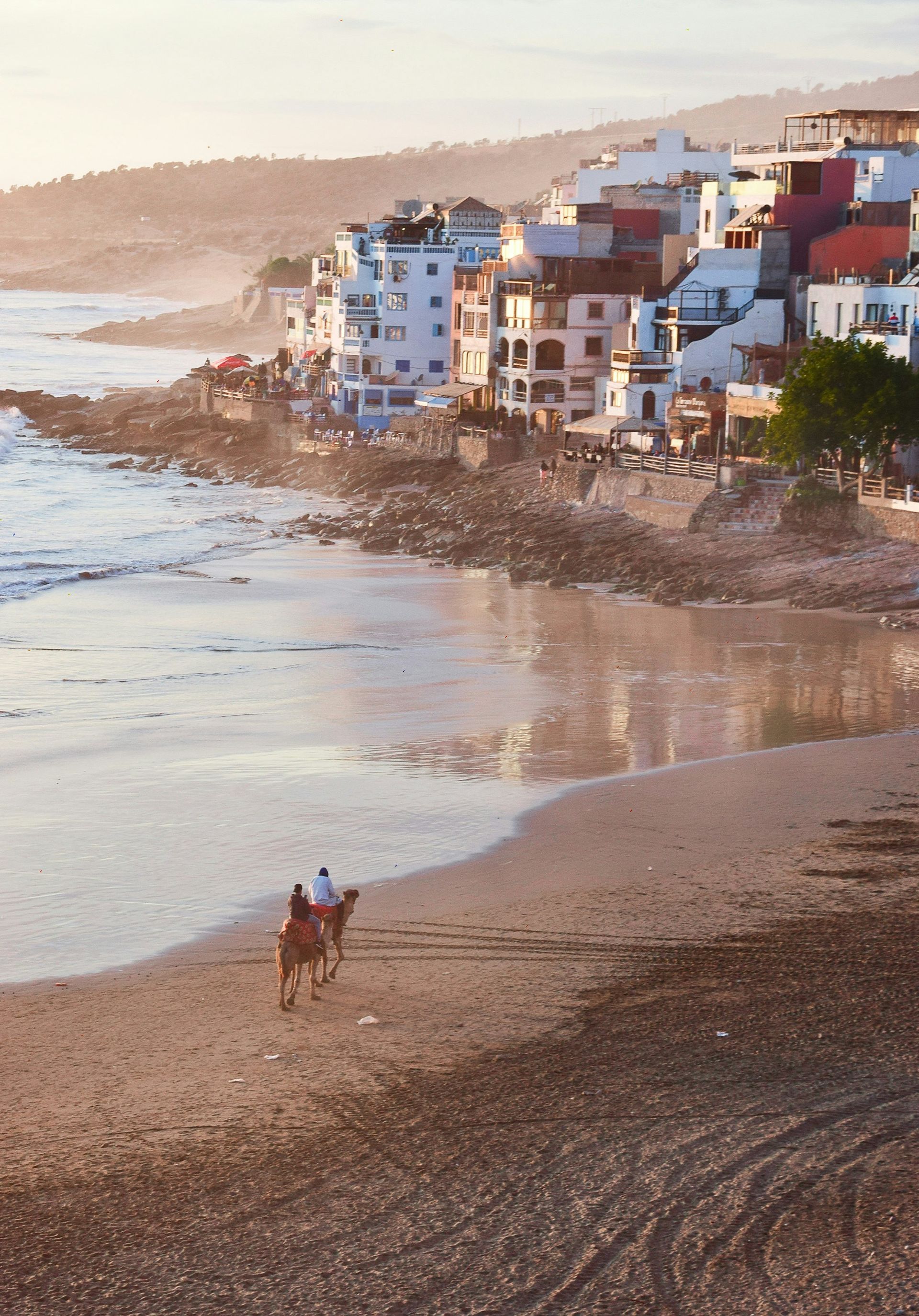 A couple riding on the back of a camel on a beach in Taghazout, Morocco.