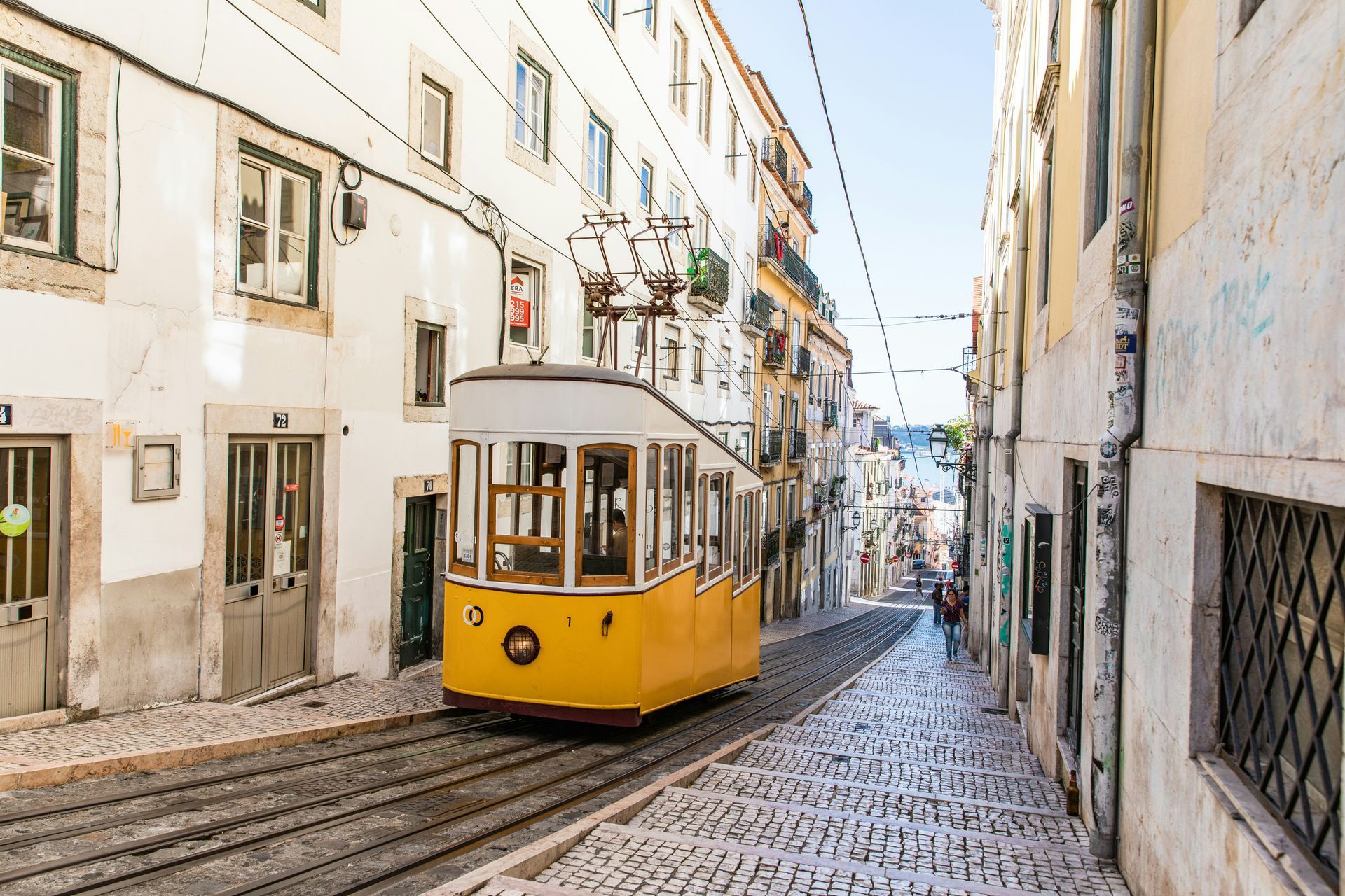 Yellow tram on cobblestone street in Lisbon, Portugal, between buildings.