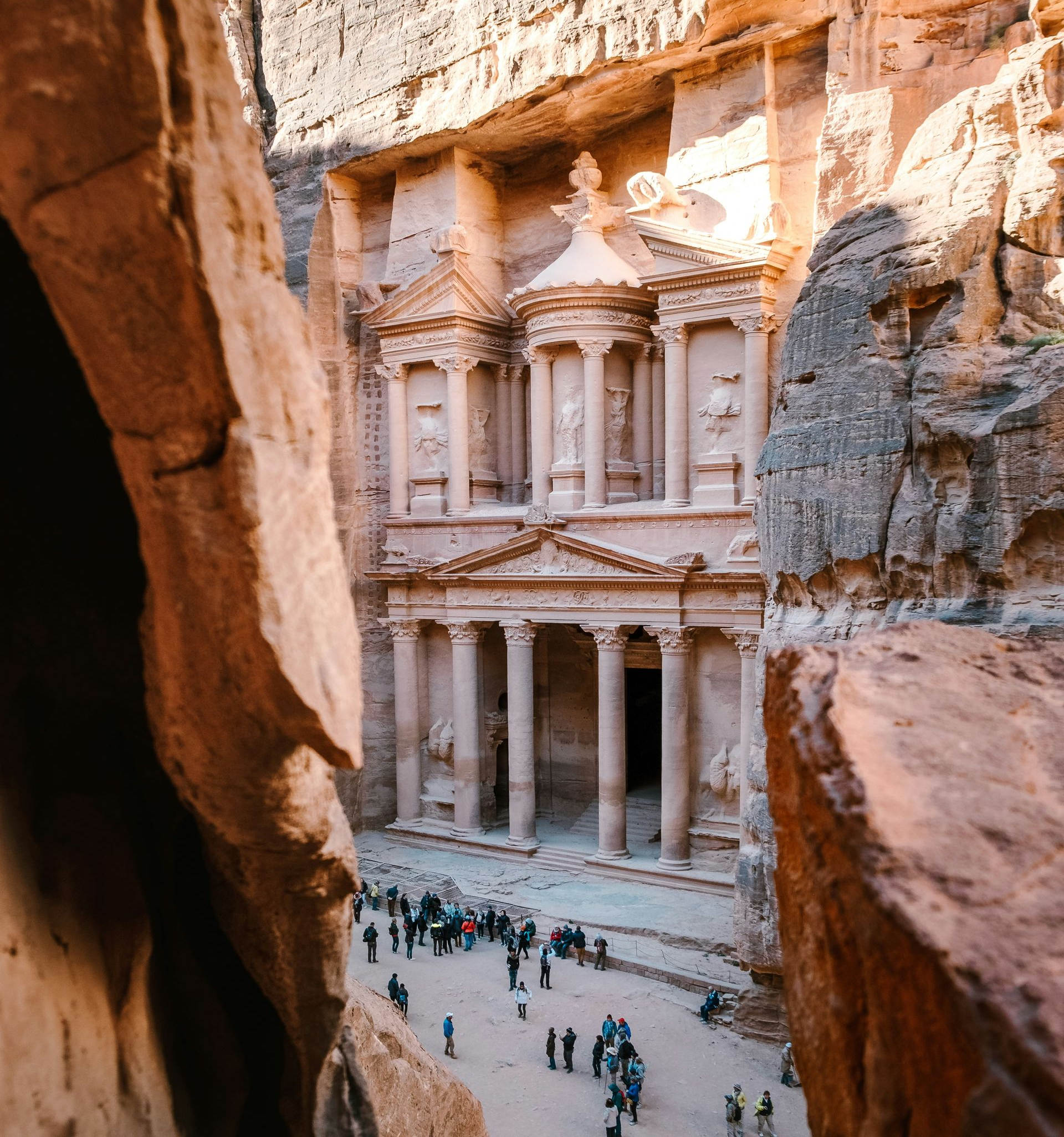 Al-Khazneh (The Treasury) in Petra, Jordan. Carved into sandstone cliffs, with columns and tourists below.