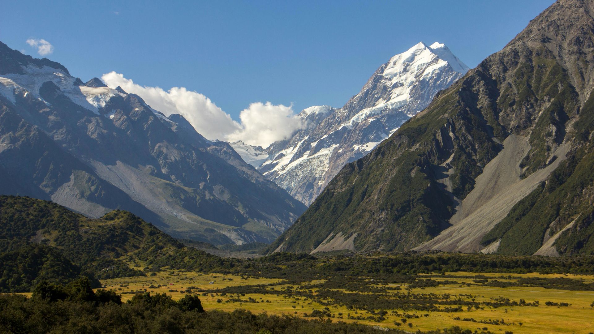 A mountain range with snow on the peaks and a field in the foreground in Mount Cook National Park, New Zealand.