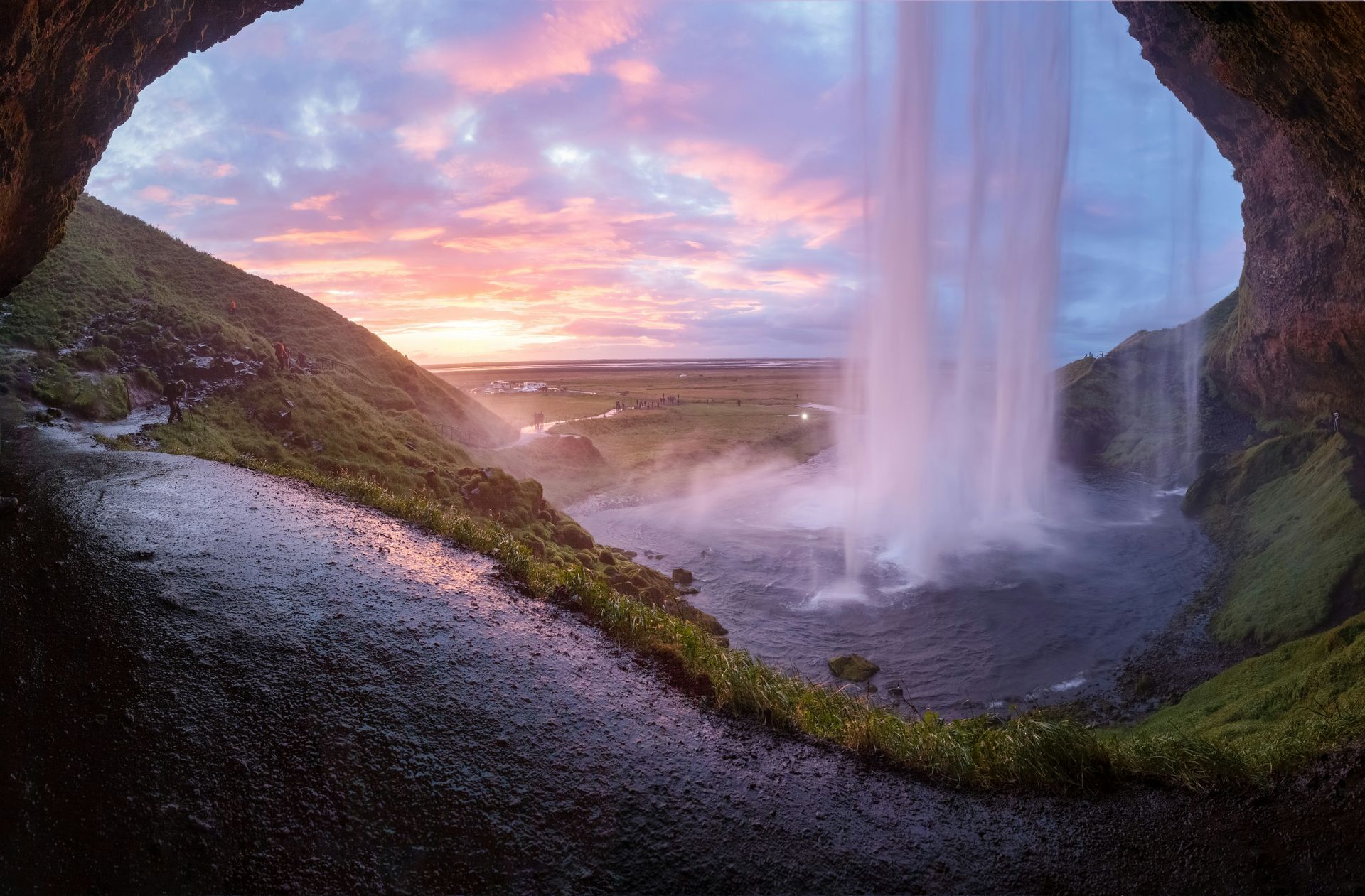 A waterfall is visible through a cave at sunset in Iceland's Golden Circle.