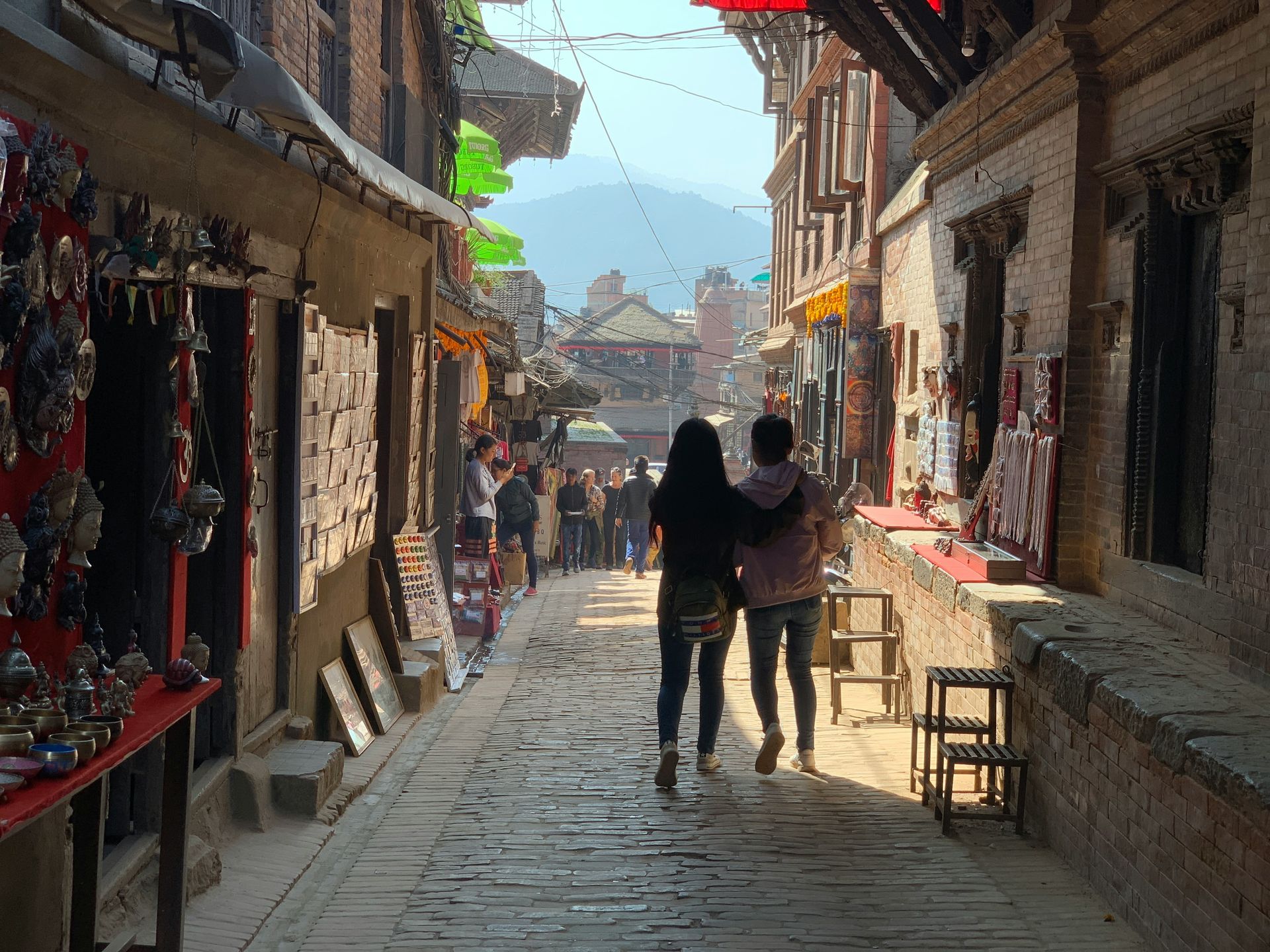 Cobblestone street lined with shops, two people walking in Bhaktapur, Nepal.