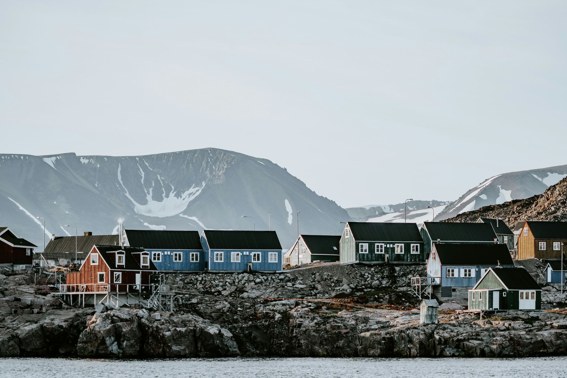 Colorful houses on a rocky coast with mountains in the background in Ittoqqortoormiit, Greenland.