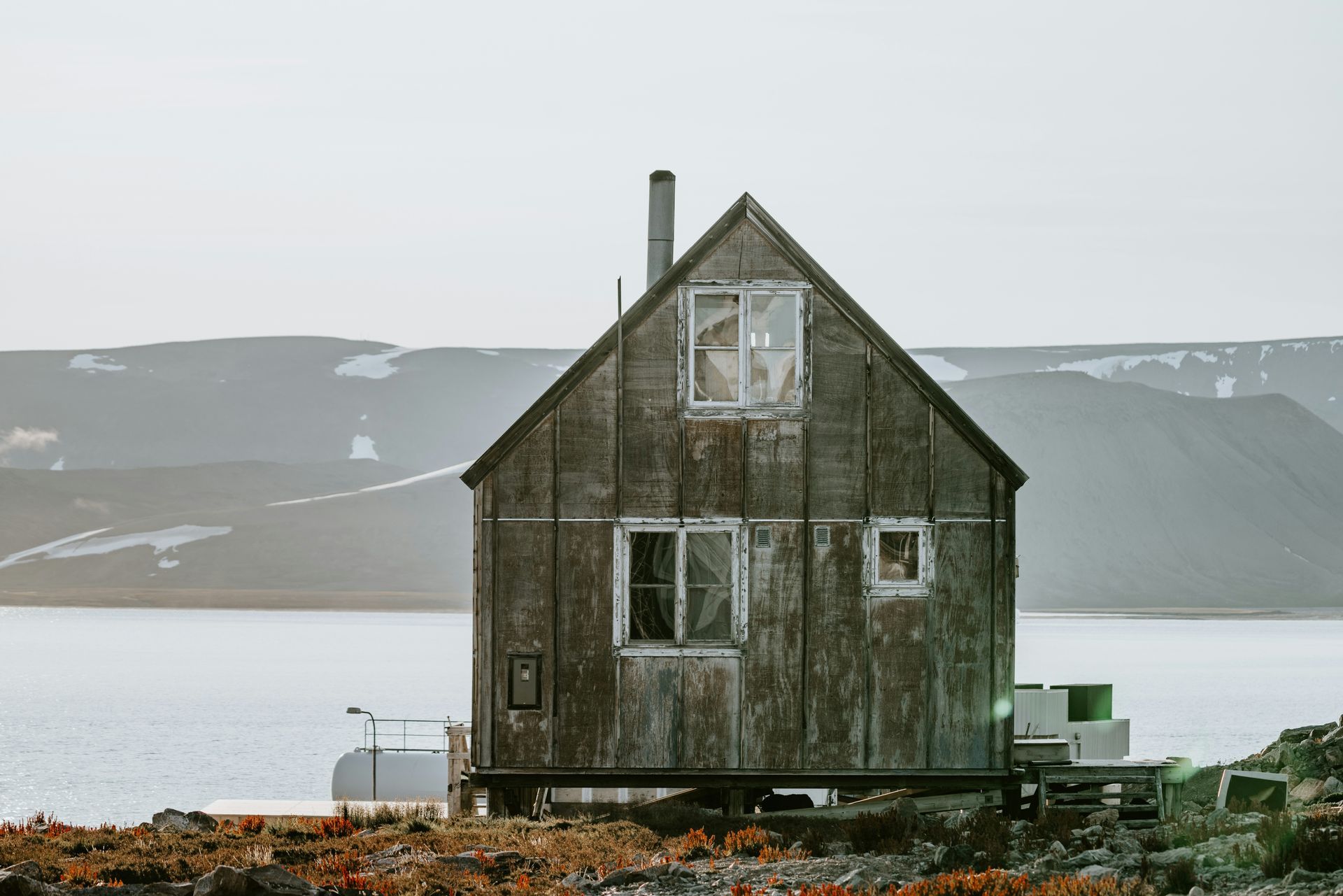 Weathered wooden cabin on rocky shore, overlooking water and mountains in Ittoqqortoormiit, Greenland.
