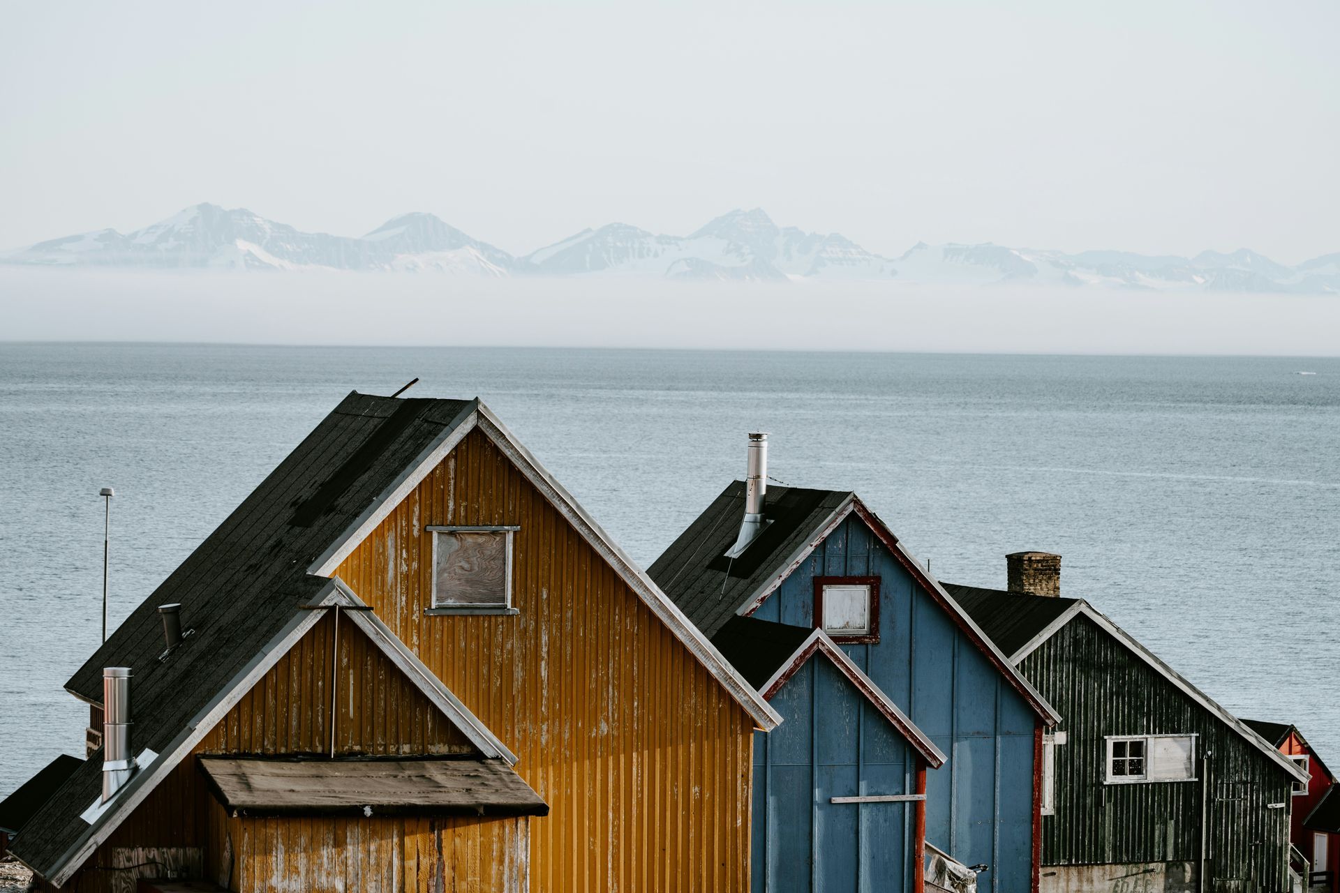 Row of colorful wooden houses by the sea, with mountains in the background in Ittoqqortoormiit, Greenland.