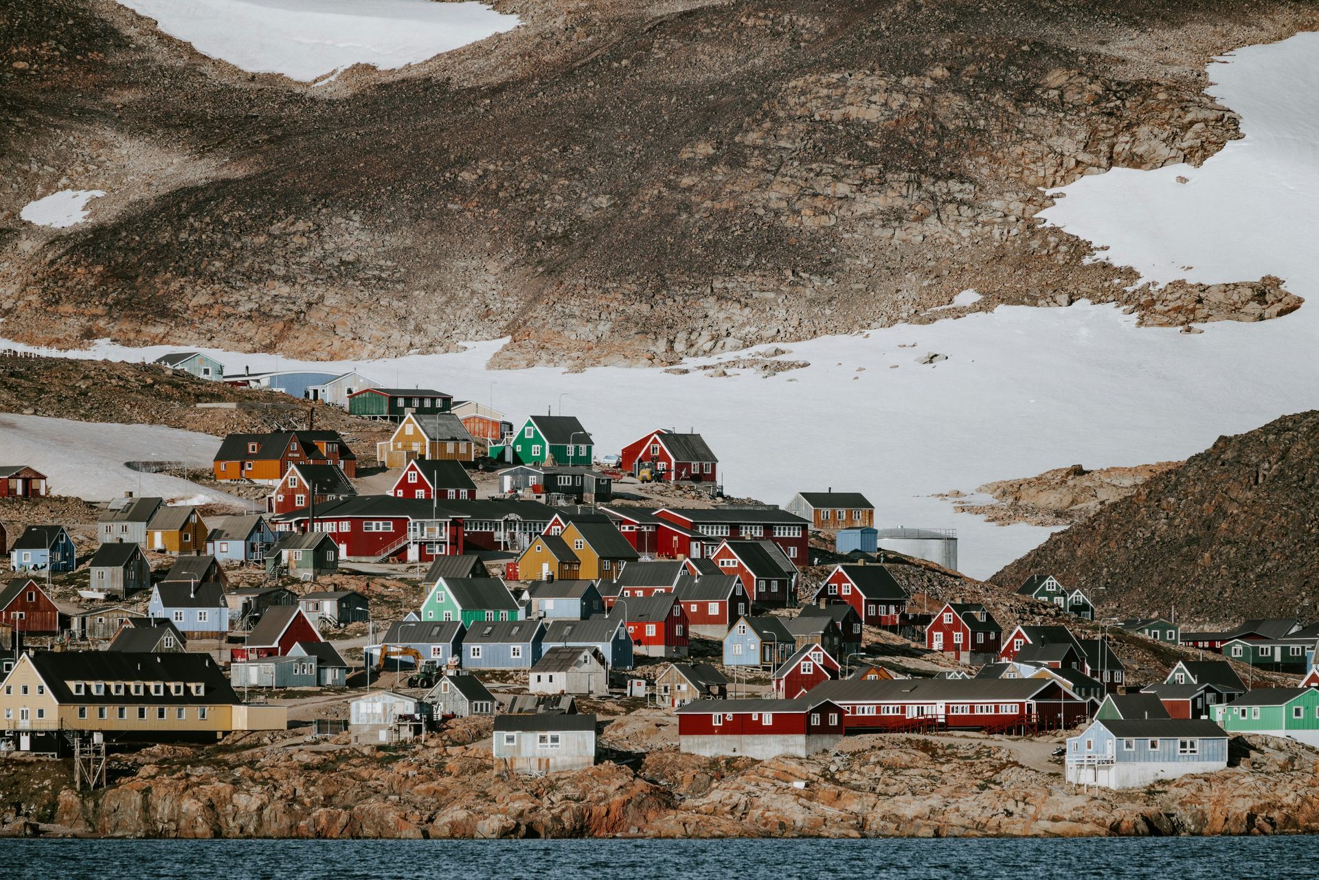 Colorful houses on a rocky hillside in the village of Ittoqqortoormiit, Greenland. Snow and mountains in the background.
