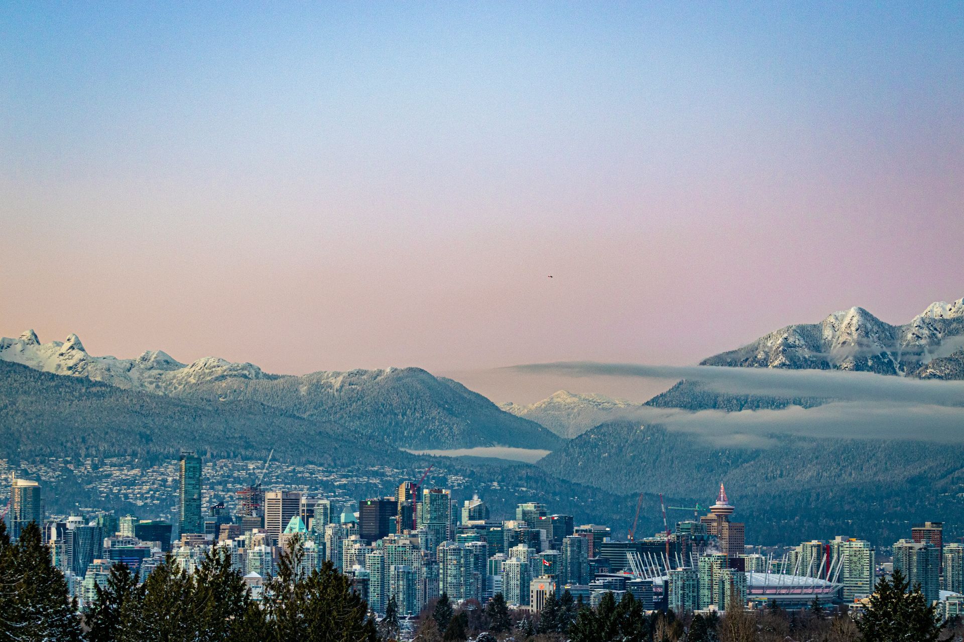Vancouver, Canada's skyline with snow-capped mountains in the background under a pastel sky.