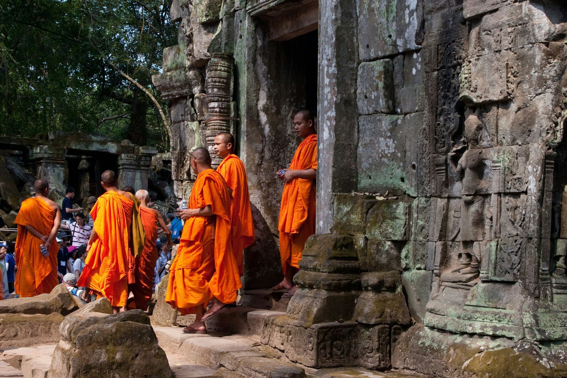 Buddhist monks in orange robes at an ancient stone temple in Cambodia.
