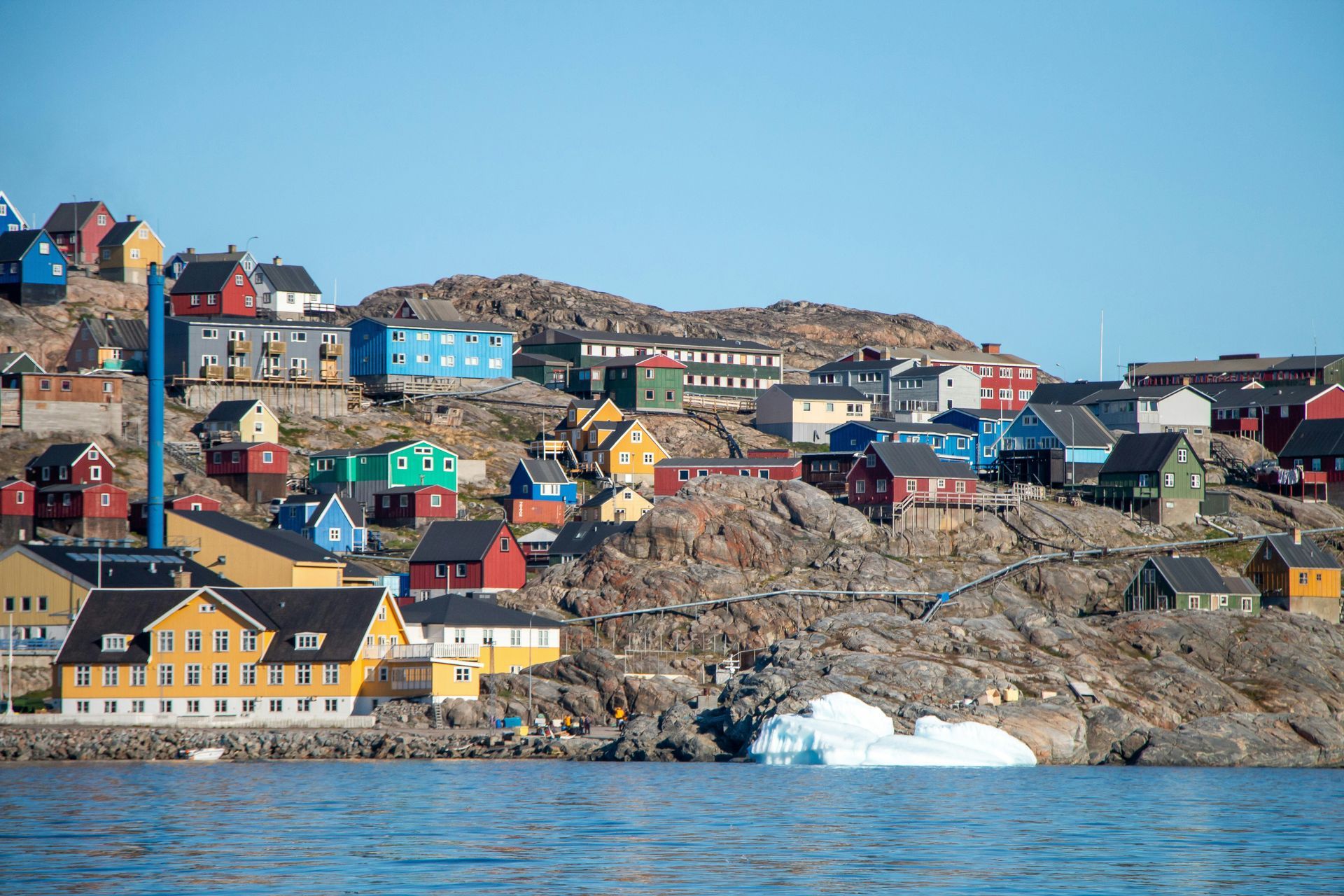 Colorful houses on a rocky hillside in a coastal town, with ice and water in the foreground in Uummannaq, Greenland.